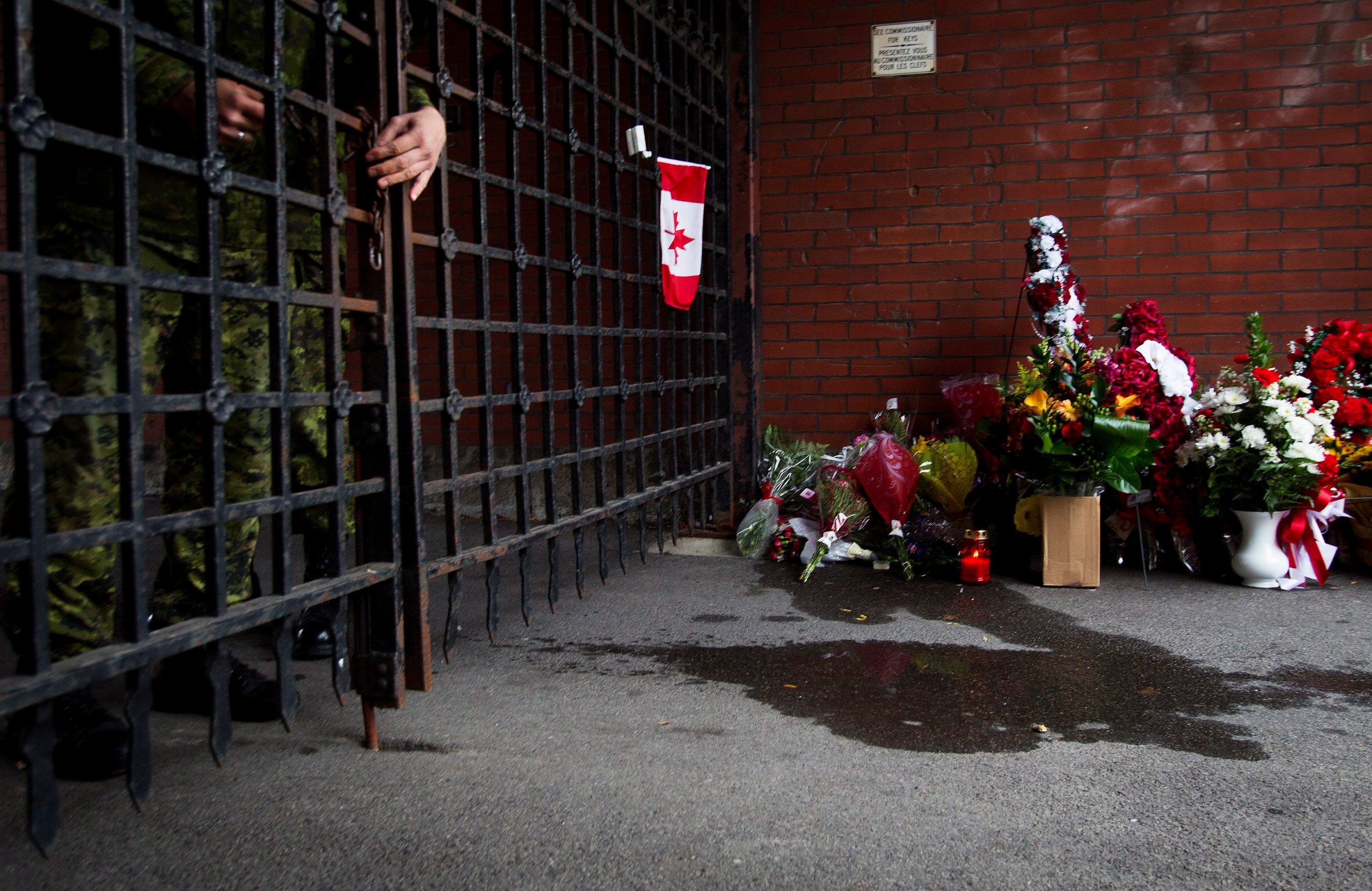 A soldier locks the gates as flowers are placed at a memorial outside the gates of the John Weir Foote Armory, the home of the Argyll and Sutherland Highlanders of Canada in Hamilton, Ontario on Oct. 22, 2014, in memory of Canadian soldier Nathan Cirillo.