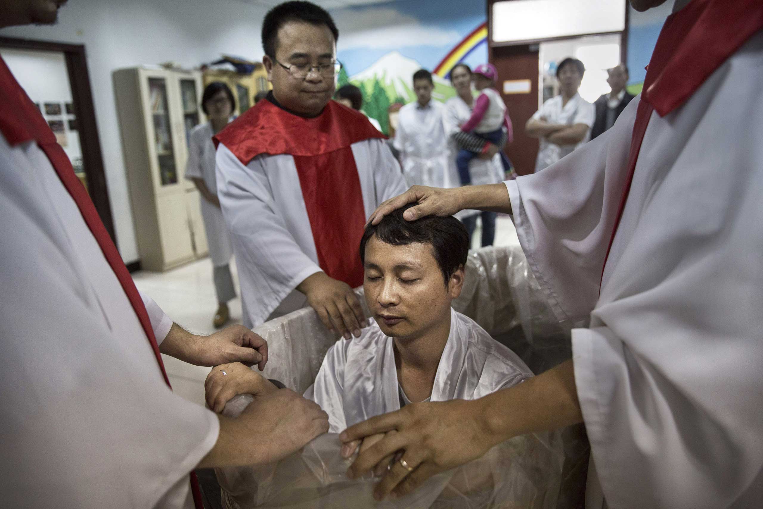 A new Christian man sits in a small tub of water as he is baptized during a ceremony.