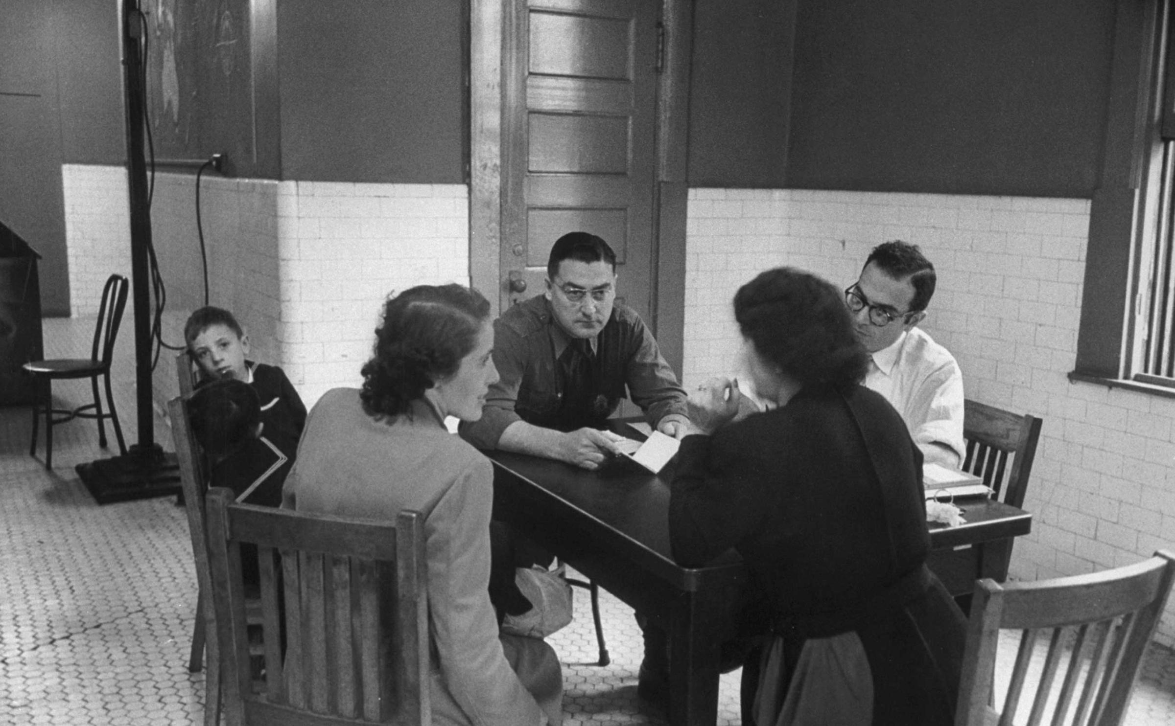 "Maria Nadalin of Italy, seated at left of the table, is worked on by an inspector-stenographer-interpreter team ..."