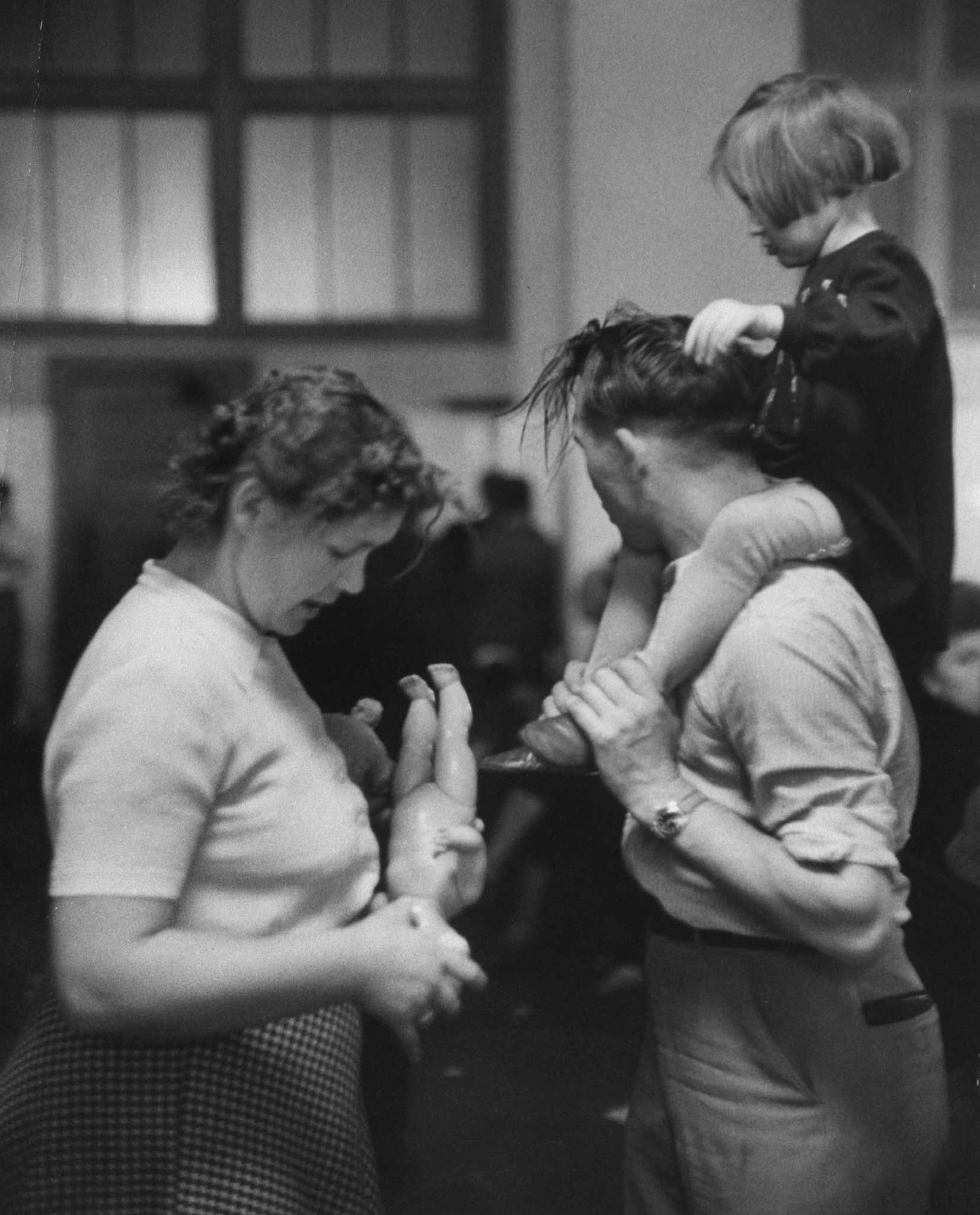 "Exhausted parents in recreation hall try to keep their child amused and quiet. Most of them will put up with endless piggyback riding, hair-pulling -- anything -- to get relief from the bewildered crying."