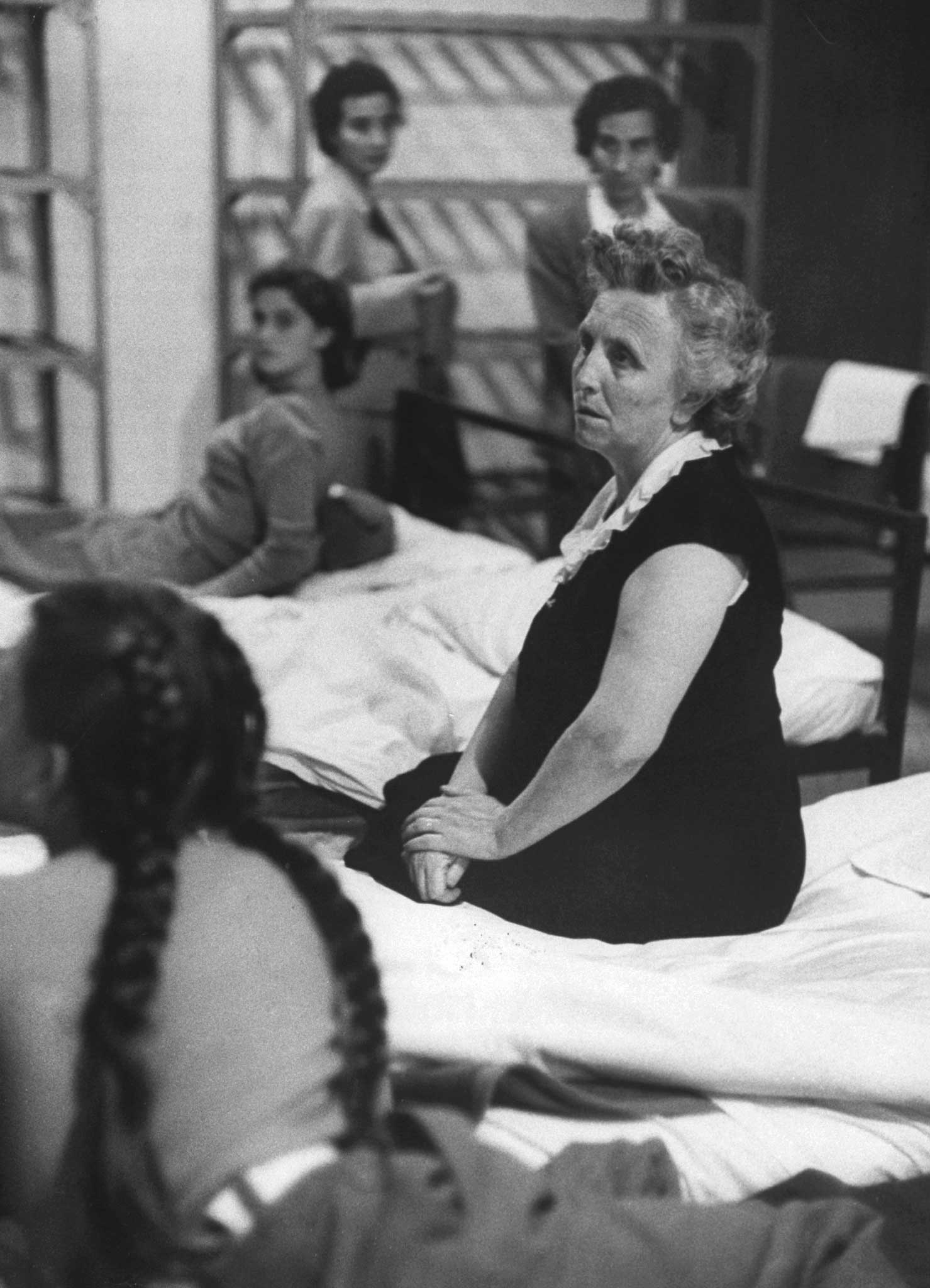 "In women's dormitory, separated from husbands, wives sit silently on their beds. At right is Maria Palmerini of Italy, here for a six-month visit. She receives same treatment as those who will stay."