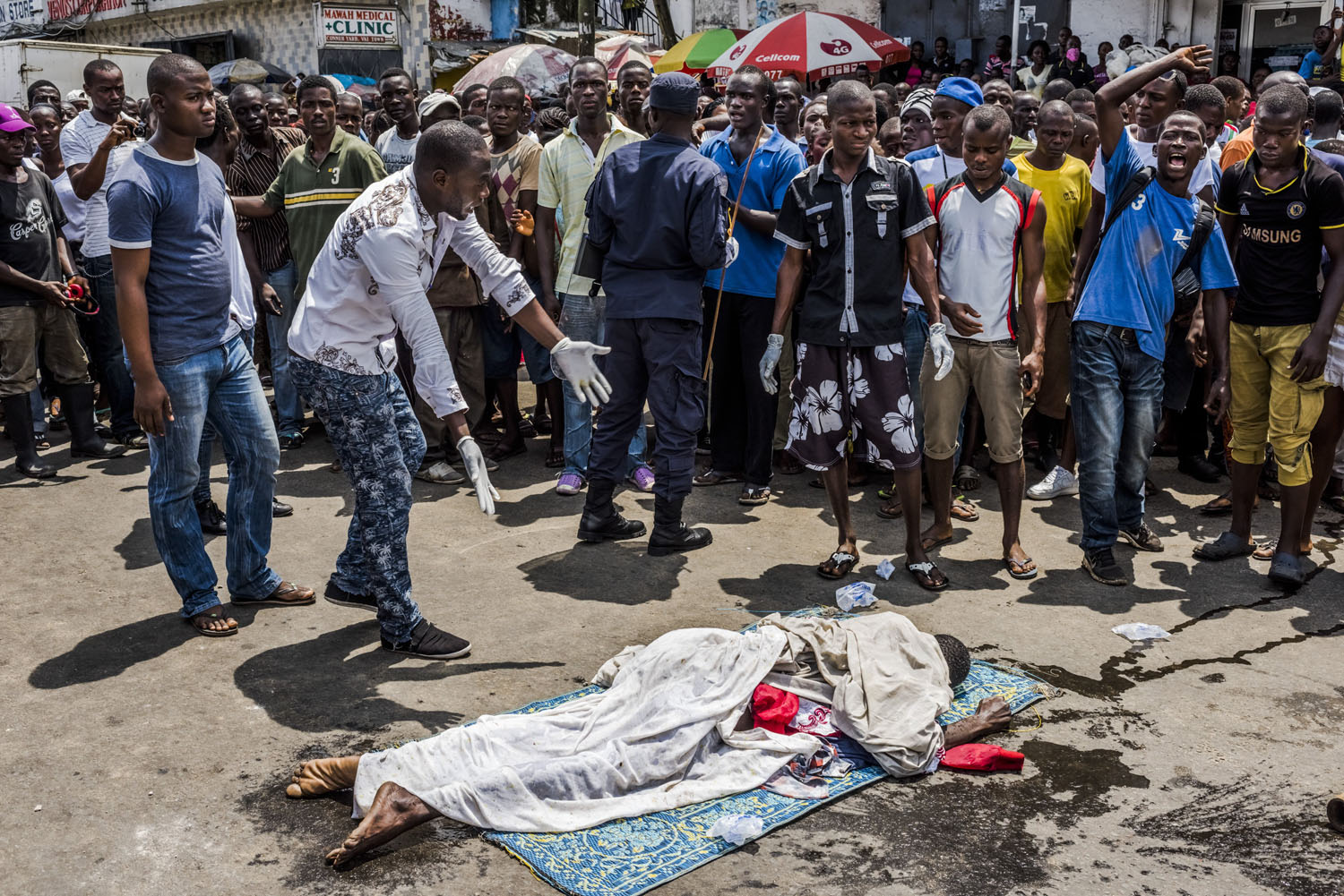 Residents look on as the body of a man suspected of dying from Ebola lies in a busy street, after it was reportedly dragged there to draw attention of burial teams following days of failed attempts by his family to have his body picked up, in Monrovia, Liberia, Sept. 15, 2014.