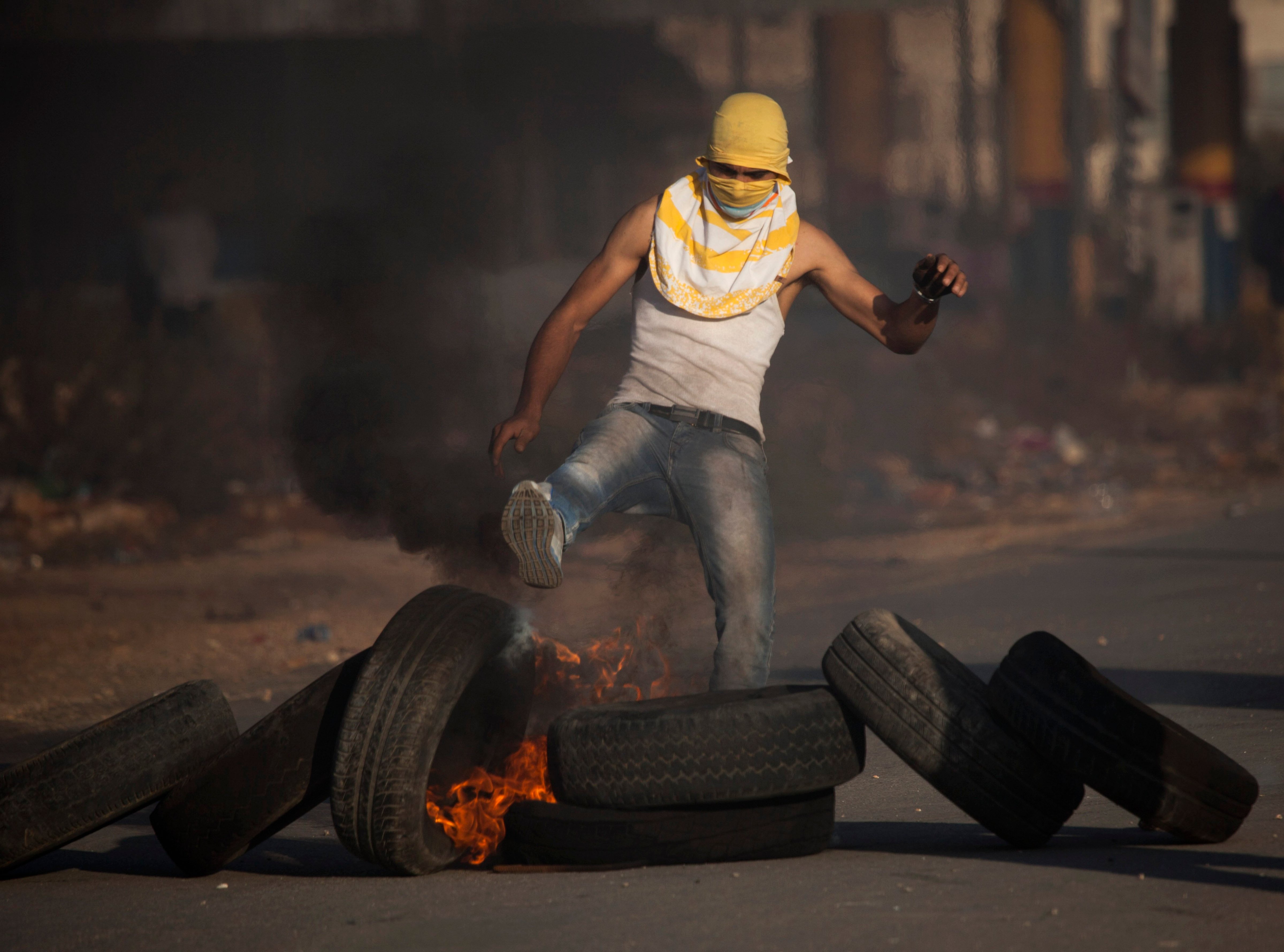 A masked Palestinian kicks a burning tire during clashes with Israeli security forces a day after 14-year-old Palestinian-American, Orwah Hammad was killed by Israeli troops during clashes, in the village of Silwad, near the West Bank city of Ramallah on Oct. 25, 2014. (Majdi Mohammed—AP)