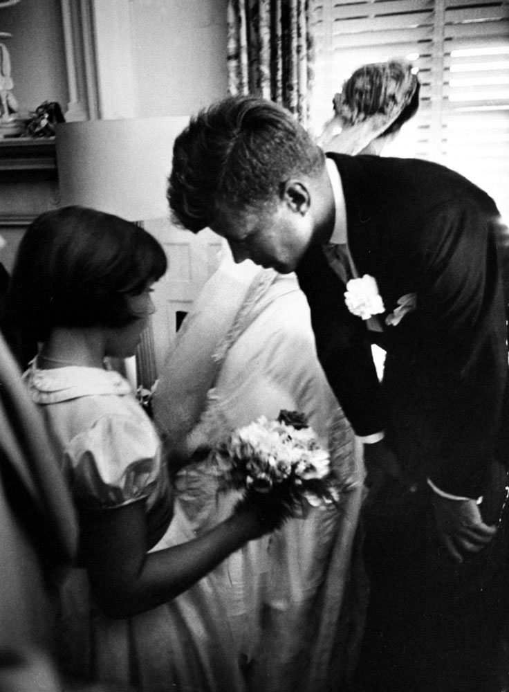 "Flower girl Janet Auchincloss, half sister of bride, talks to Kennedy while bride looks out window at guests waiting to go through receiving line."