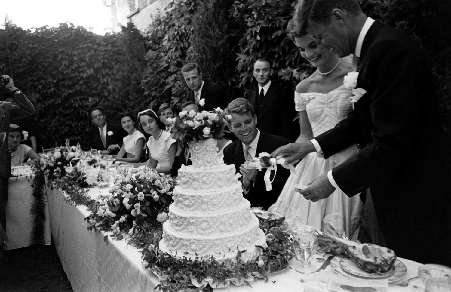 Guests, including Robert Kennedy, watch as newly married John and Jackie Kennedy cut their wedding cake, Newport, R.I., Sept. 12, 1953.