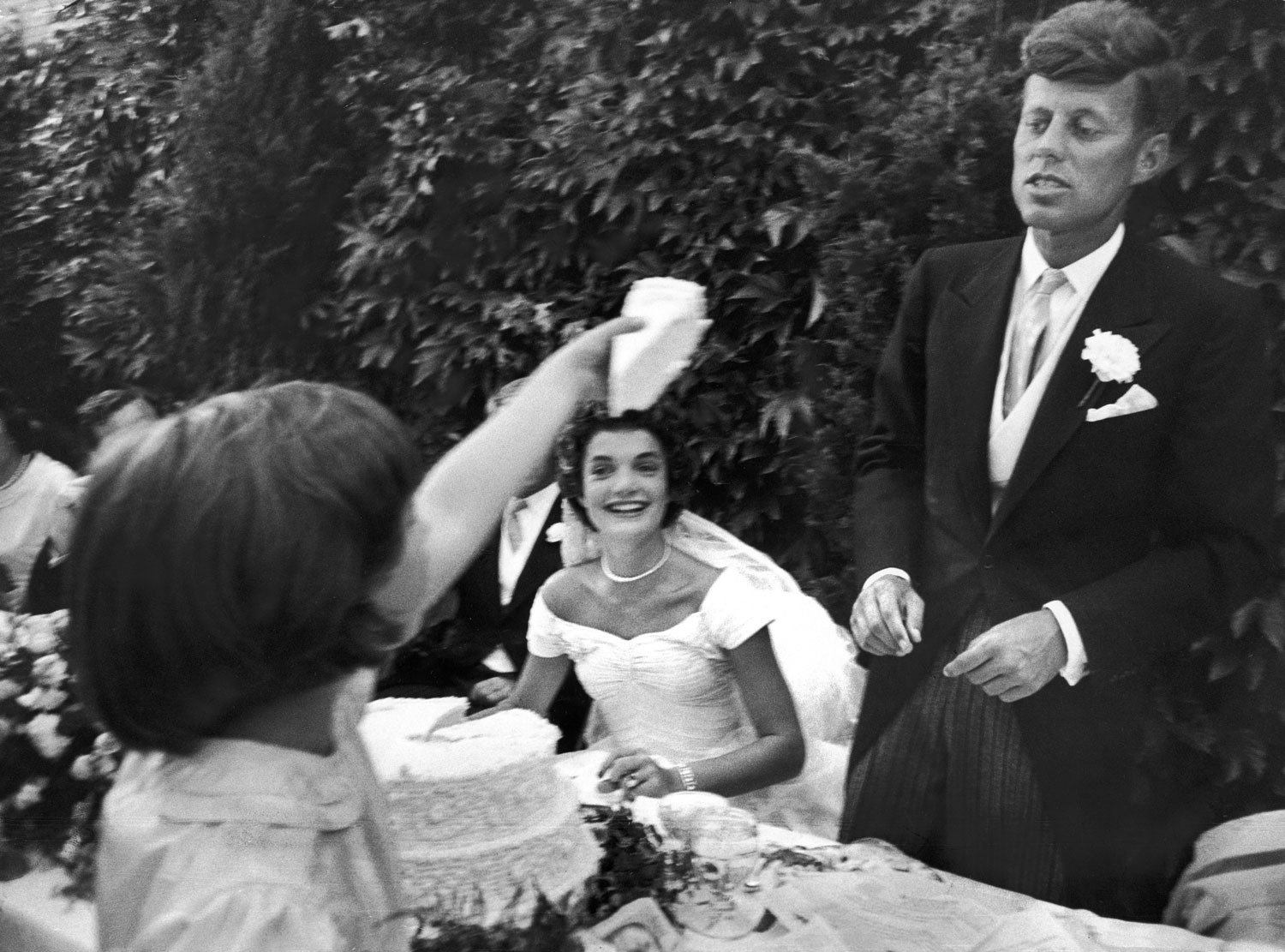 "Slice of wedding cake is offered bridegroom by flower girl Janet at the luncheon. Kennedy had already had some cake so did not want any more."