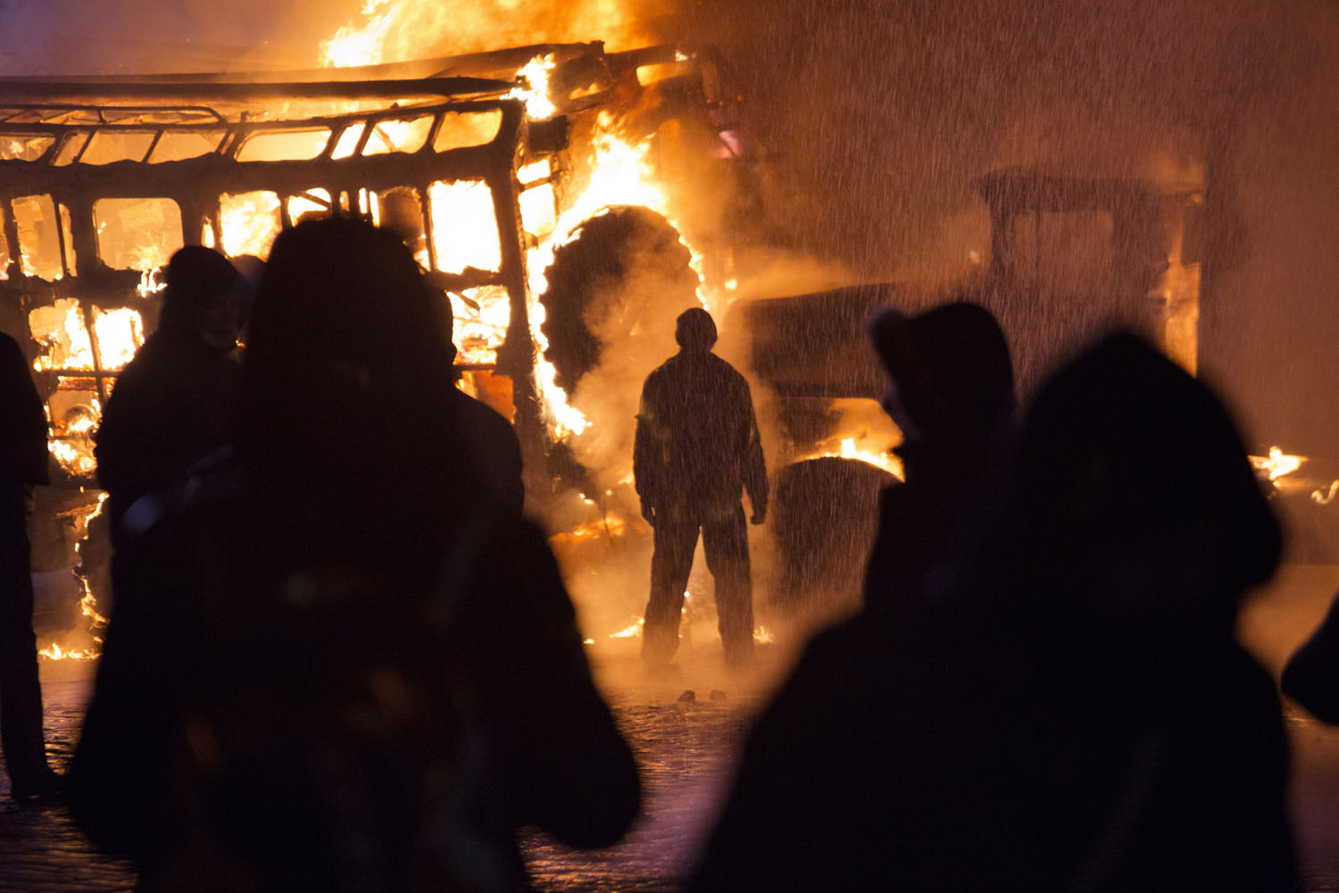 A demonstrator stands in front of burning vehicles during violent clashes with police near Hrushevsky Street, Jan. 19, 2014.