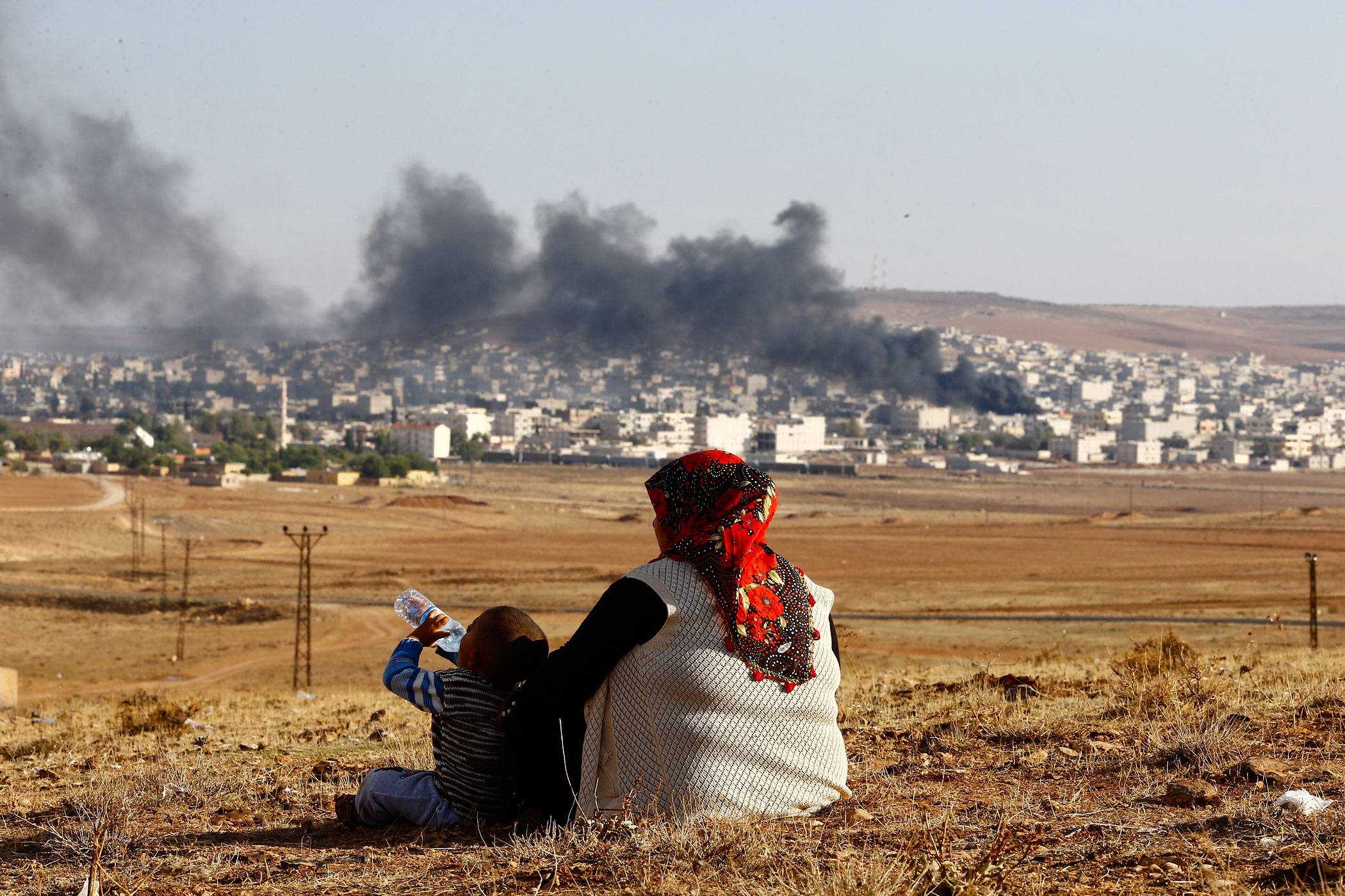 Turkish Kurds watch smoke rises over Syrian town of Kobani after an airstrike, as seen from the Mursitpinar border crossing on the Turkish-Syrian border