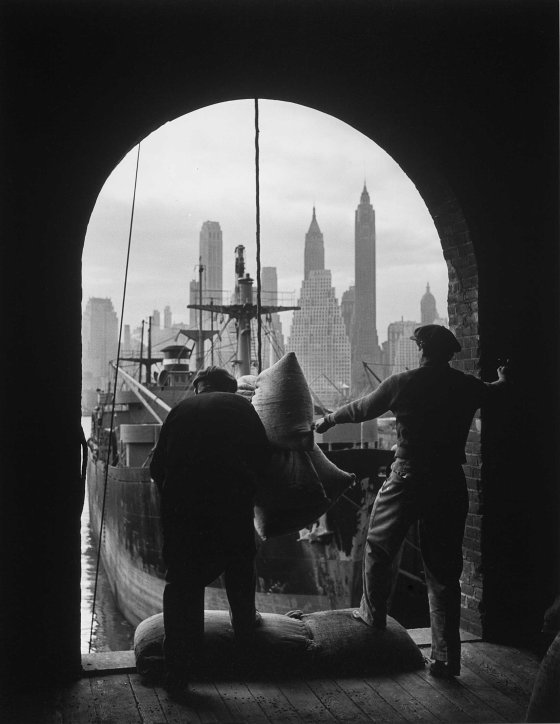 Men unload coffee at a Brooklyn dock with Lower Manhattan visible in the background, 1949.