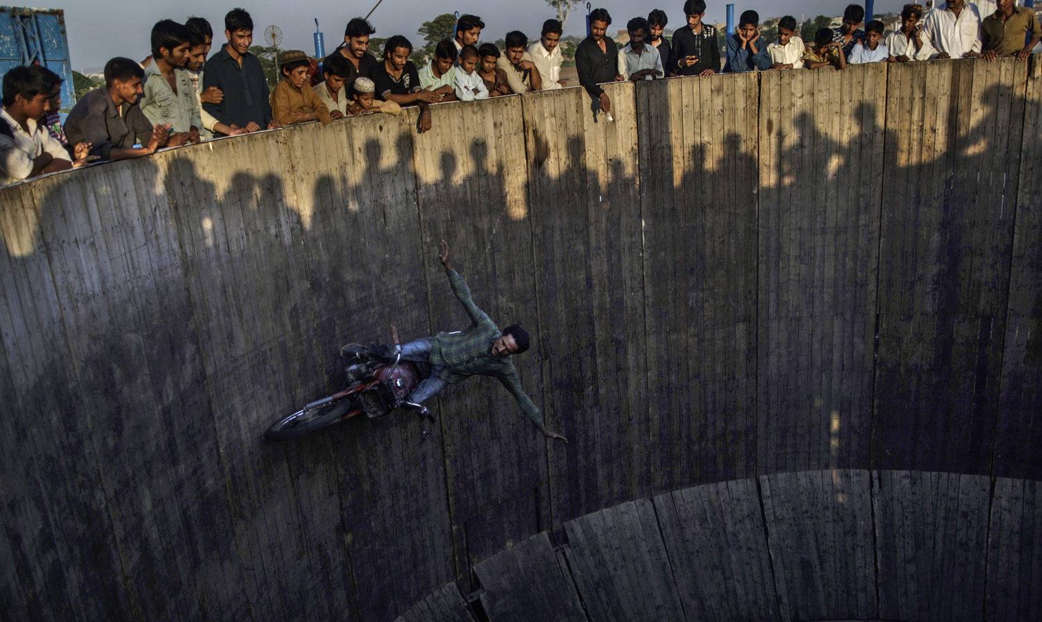 Pakistanis watch as an acrobat rides his motorcycle around a circular track, at an entertainment park set up outside a shrine in Rawalpindi, Pakistan, June 19, 2013.