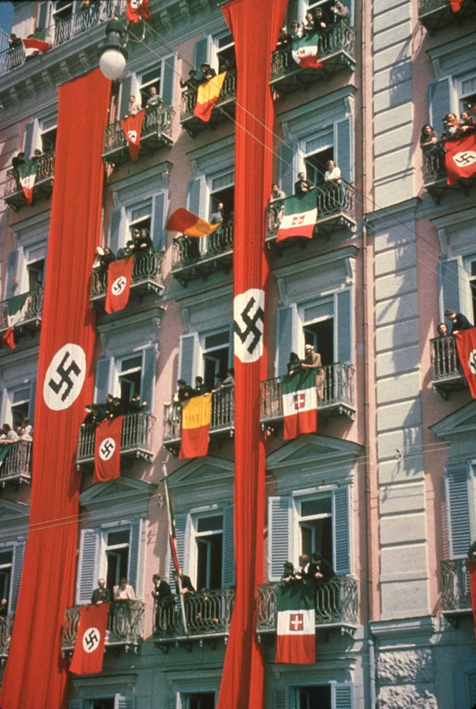 Nazi and Italian flags draped from balconies to welcome Adolf Hitler during state visit to Italy, 1938.
