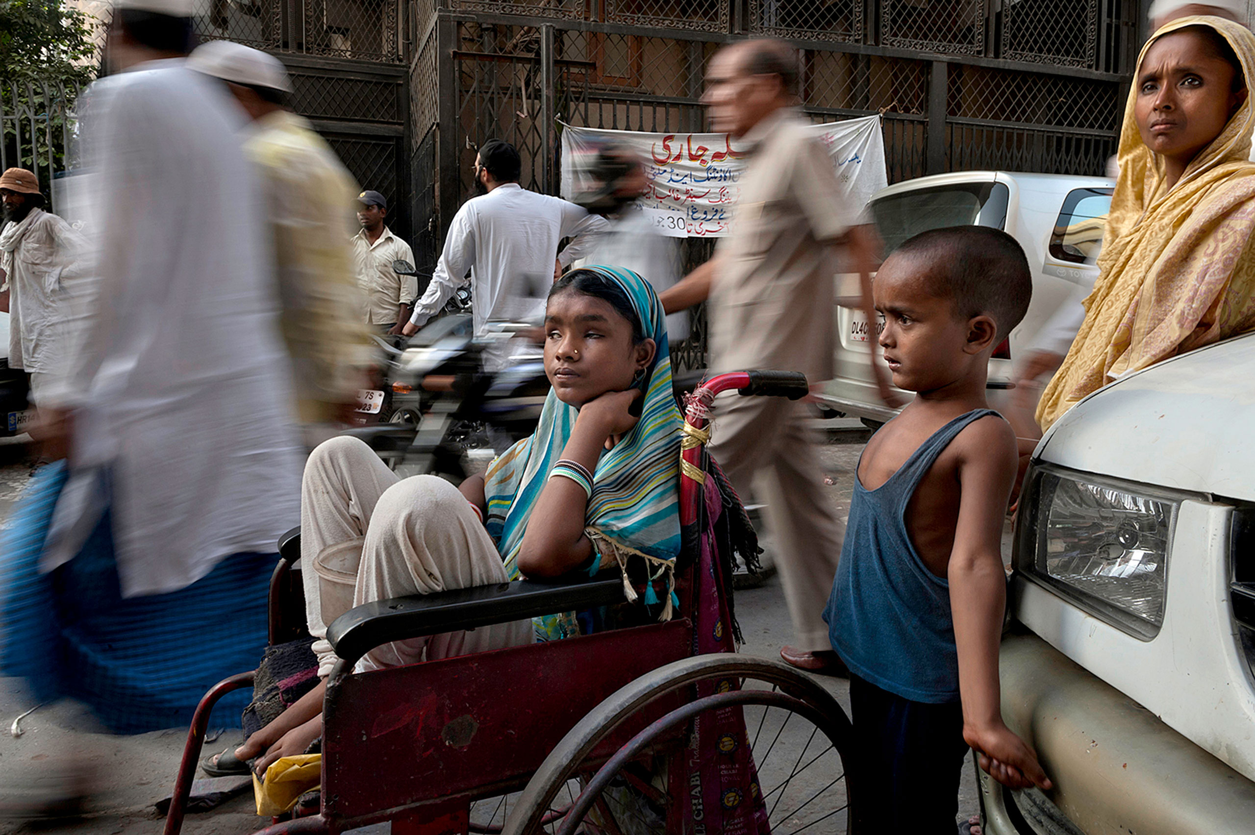 A sea of people passes by Hunupa Begum, 13, who has been blind for the past 10 years and lives close to the Nizamudin Bangala Masjid (Mosque) in New Delhi, India. She begs as the only source of income for her family that consist of a brother Hajimudin Sheikh, 6, center, who suffers fluids that accumulate in his head and her mother Manora Begum, 35, right, who suffers from Asthma, and she has a womb ailment and can't do manual labor. Their father Nizam Ali Sheikh died ten years ago of Tuberculosis. Her wheelchair was donated by a passerby.