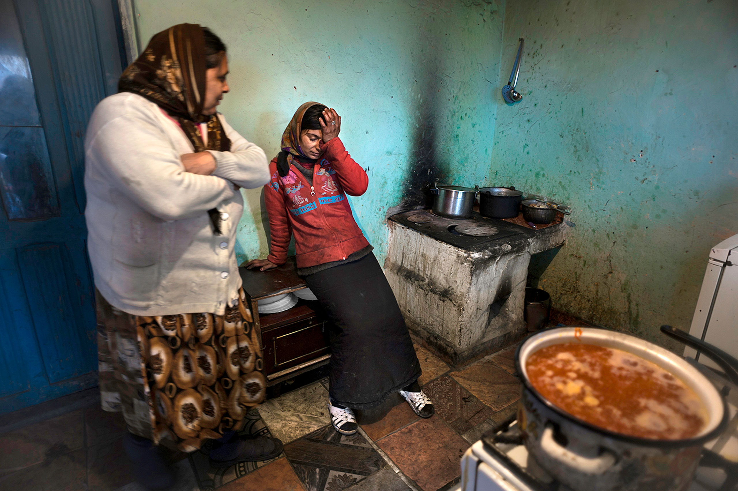 Complaining of stomach pains Viorica Gulie, 31, takes a break from cooking soup for her family as her mother-in-law Constanta Gulie, 58,  looks on at left.  She suffers from Gastitis of her stomach.  With no money for medication or to go to the hospital she has to live in pain. Their house which has no running water or a bathroom is built on state land and they don't have title deeds so they are in fear of being evicted in Slatina, Romania.