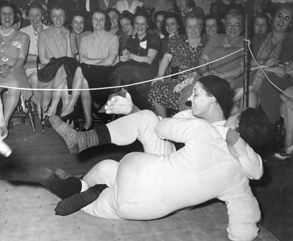 LIFE on the battle: "Huffing and puffing, they punish the mat." Joan Thornwaite (back to camera) "won by tickling in five minutes." Note: Her opponent's mustache is attached to her face with chewing gum.
