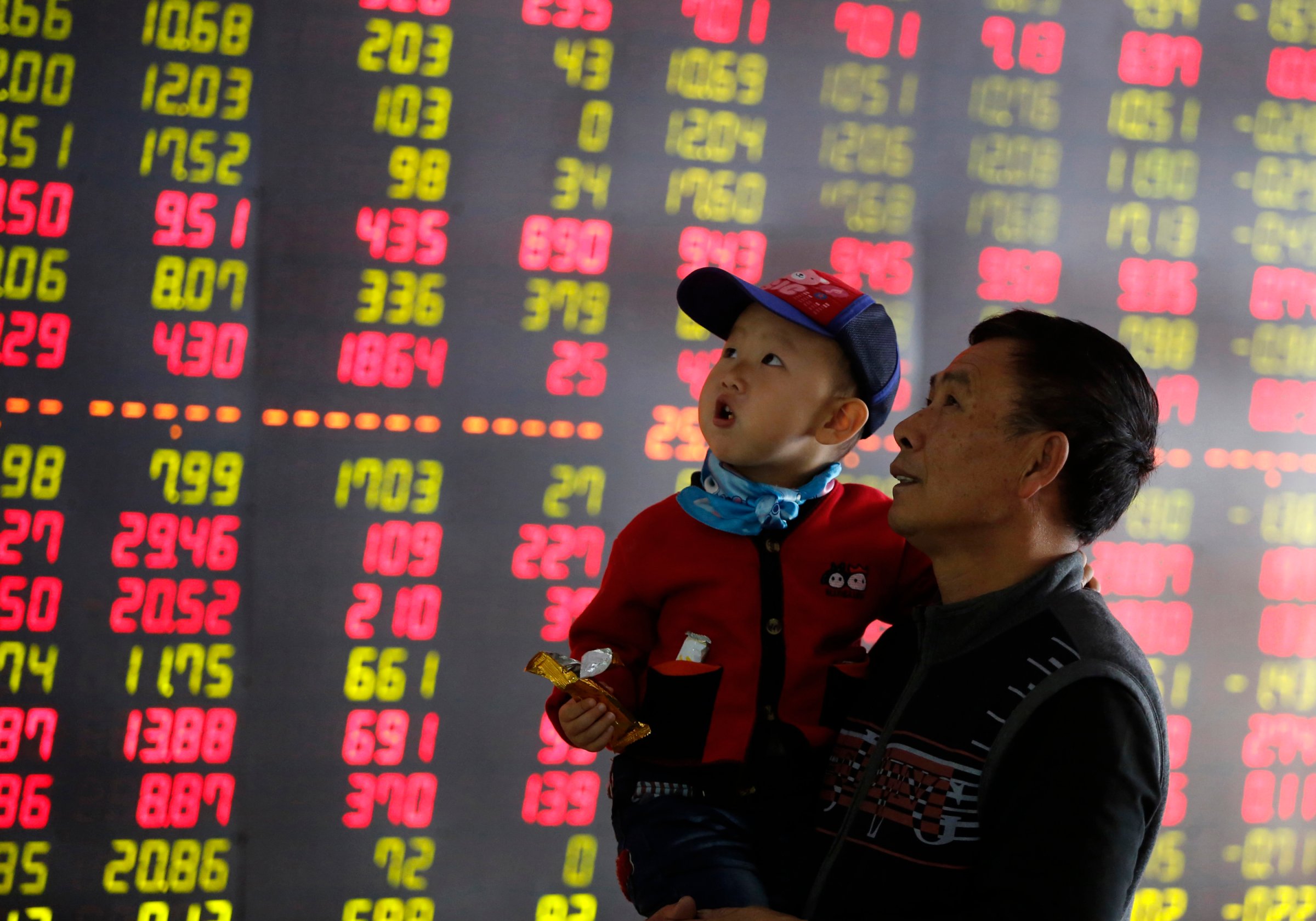 An investor holds a child in front of an electronic screen showing stock information at a brokerage house in Shenyang