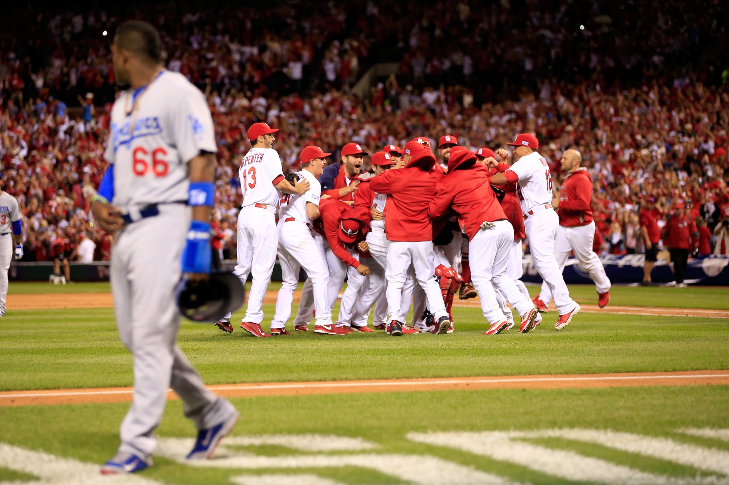 The St. Louis Cardinals celebrate after defeating the Los Angeles Dodgers as Yasiel Puig of the Los Angeles Dodgers walks off the field in Game Four of the National League Divison Series at Busch Stadium on Oct. 7, 2014 in St Louis.