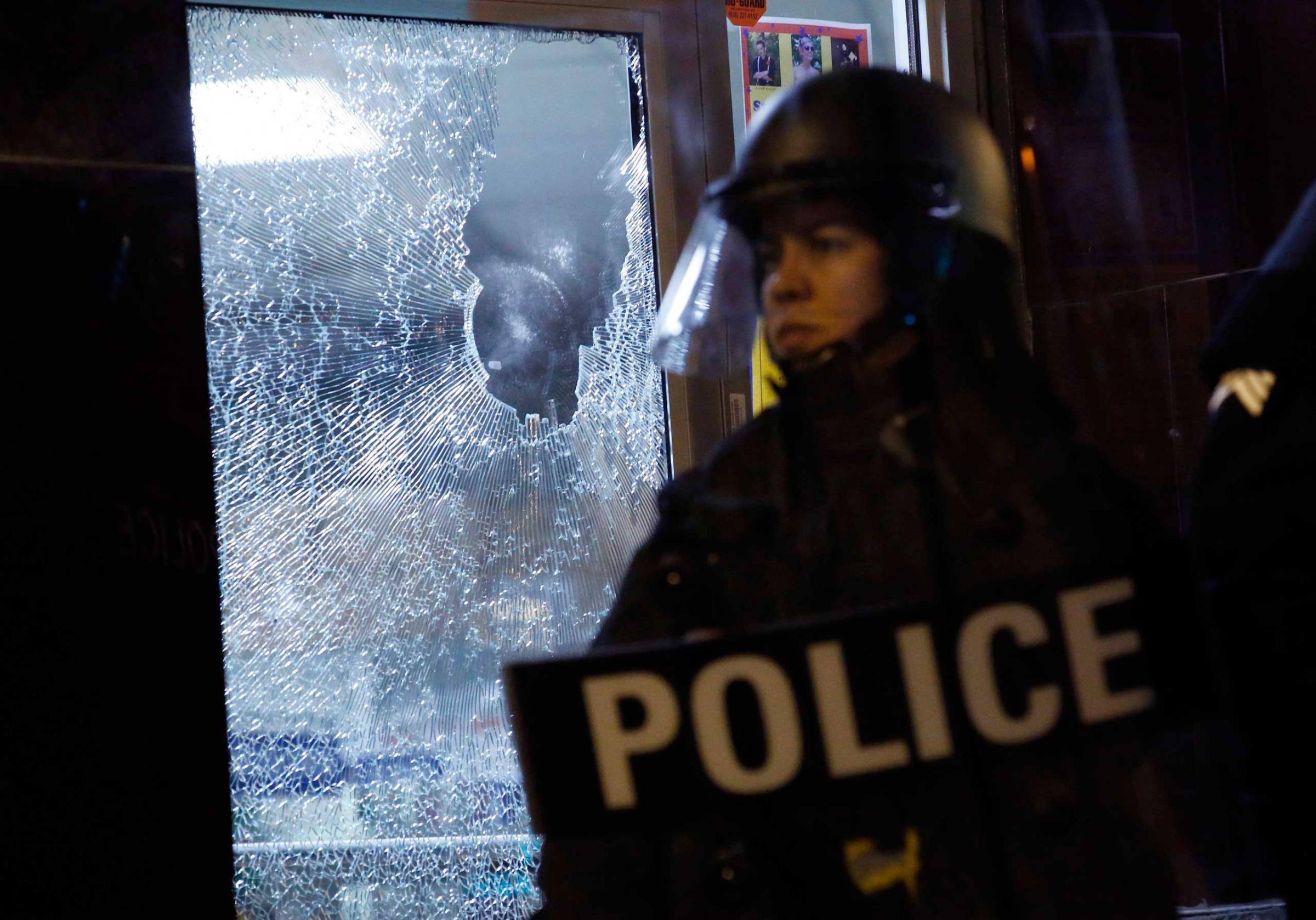 Police officer stands guard in front of a damaged storefront during a protest after a vigil in St. Louis, Missouri