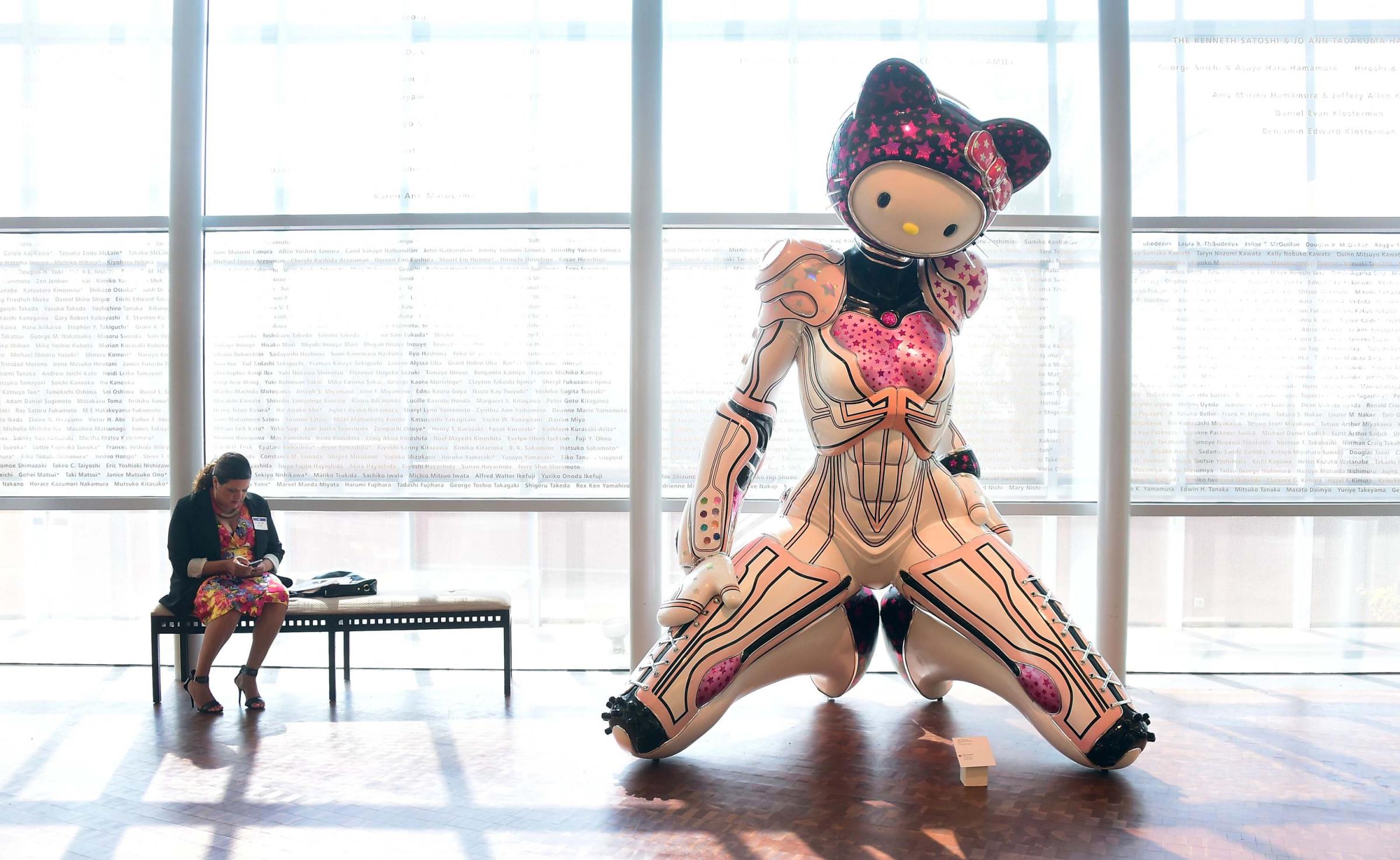 A woman is seated beside a display of "Super Space Titan Kitty", a 2014 fiberglass sculpture by Colin Christian displayed at a press event ahead of the opening of the first ever Hello Kitty exhibition in North America at the Japanese American National Museum in Los Angeles on Oct. 10, 2014.