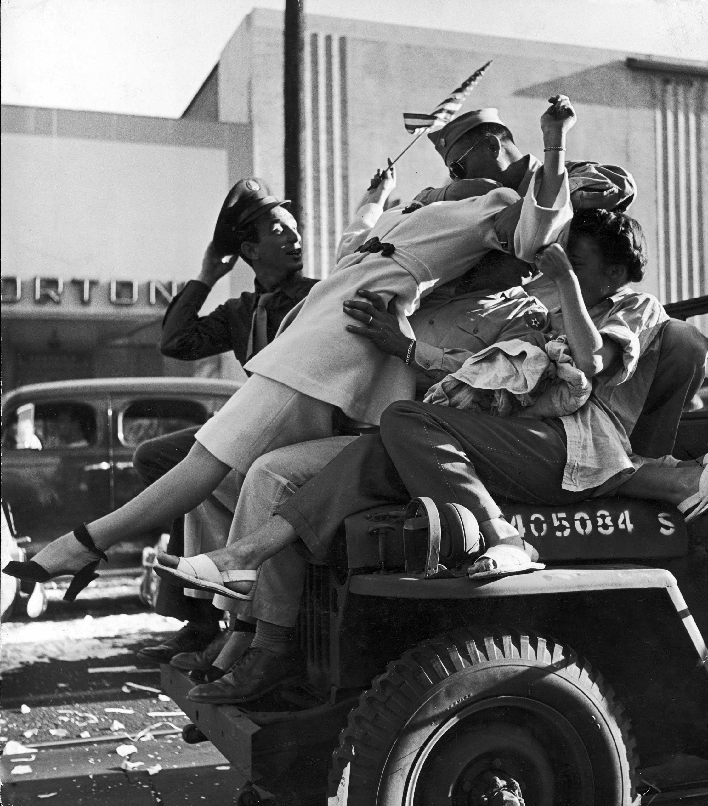 "On Hollywood Boulevard in Los Angeles carousing servicemen neck atop the hood of a careening jeep. The city rocked with joy as impromptu pedestrian parades and motor cavalcades whirled along, hindered only by hurled whiskey bottles, amorous drunks and collisions."