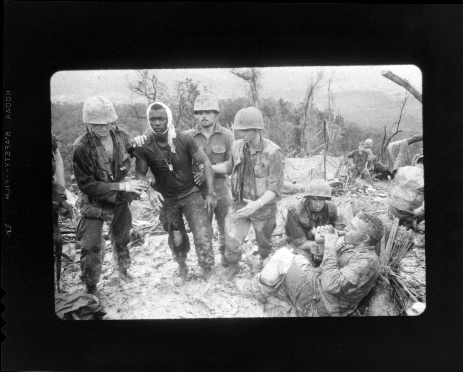 A black-and-white negative of a color image, depicting the scene on Hill 484 a few moments after Larry Burrows shot the picture that would become known as Reaching Out.