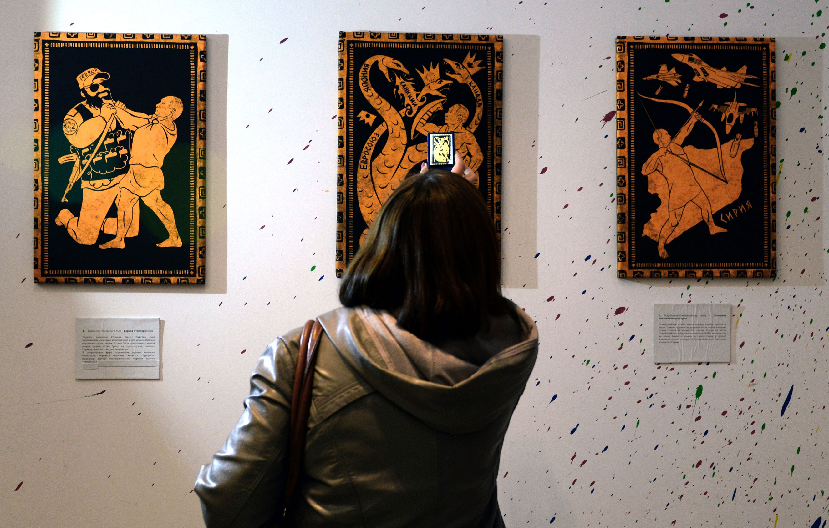 A visitor takes photos of the paintings during the "12 Labours of Putin" art exhibition on Oct. 6, 2014 marking the 60th birthday of Russia's President Vladimir Putin at the design workshop in Moscow. (Vasily Maximov—AFP/Getty Images)