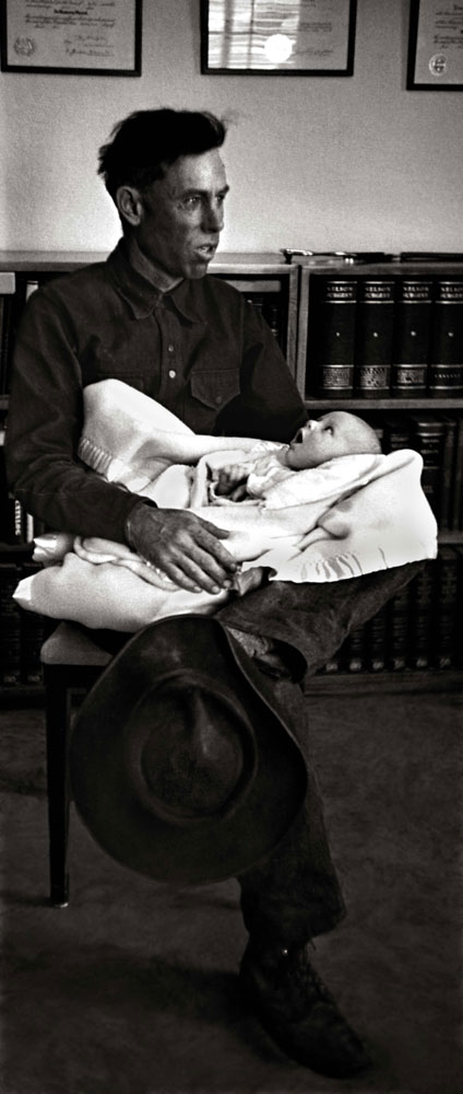 Ralph Pickering holds his 5-week-old baby while waiting to be Dr. Ceriani's first patient of the day. Pickering, a horseback guide to tourists coming to see the majestic Rocky Mountains, traveled from an outlying ranch to reach the doctor's office.