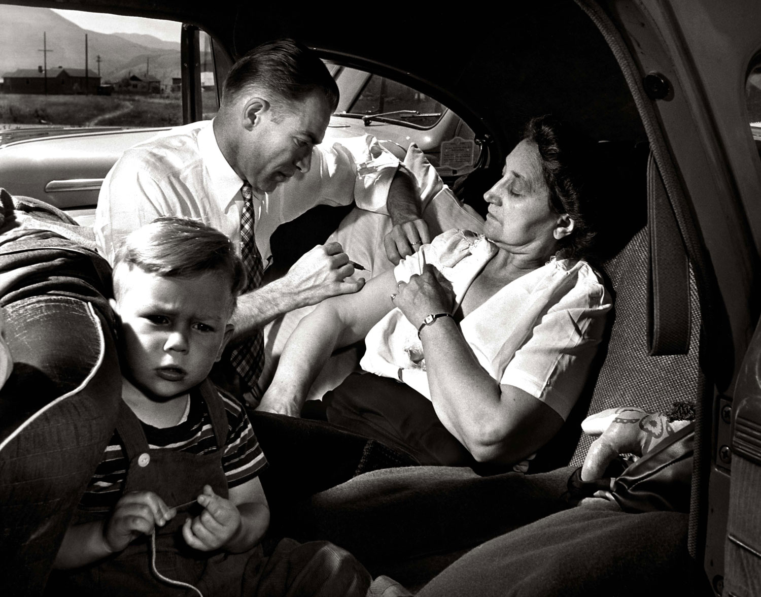 In the backseat of a car, Dr. Ceriani administers a shot of morphine to a 60-year-old tourist from Chicago, seen here with her grandson, who was suffering from a mild heart disturbance.