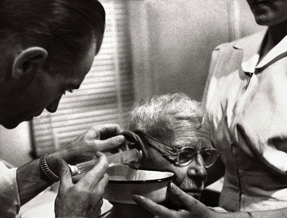 Dr. Ceriani uses a syringe to irrigate wax from an elderly man's ear to improve his hearing.