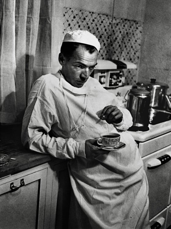 After finishing a surgery that lasted until 2 AM, Dr. Ceriani stands exhausted in the hospital kitchen with a cup of coffee and a cigarette. 