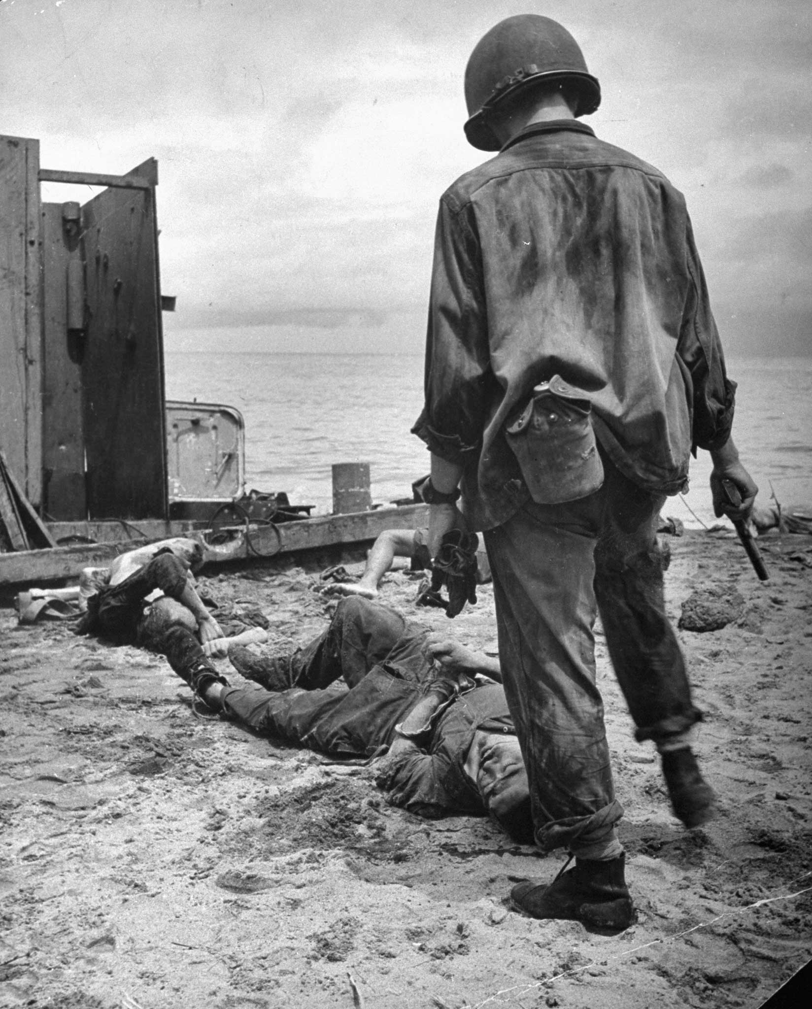 "An American soldier stands over a dying Jap whom he has just been forced to shoot. The Jap had been hiding in the landing barge, shooting at U.S. troops." New Guinea Campaign, 1942.