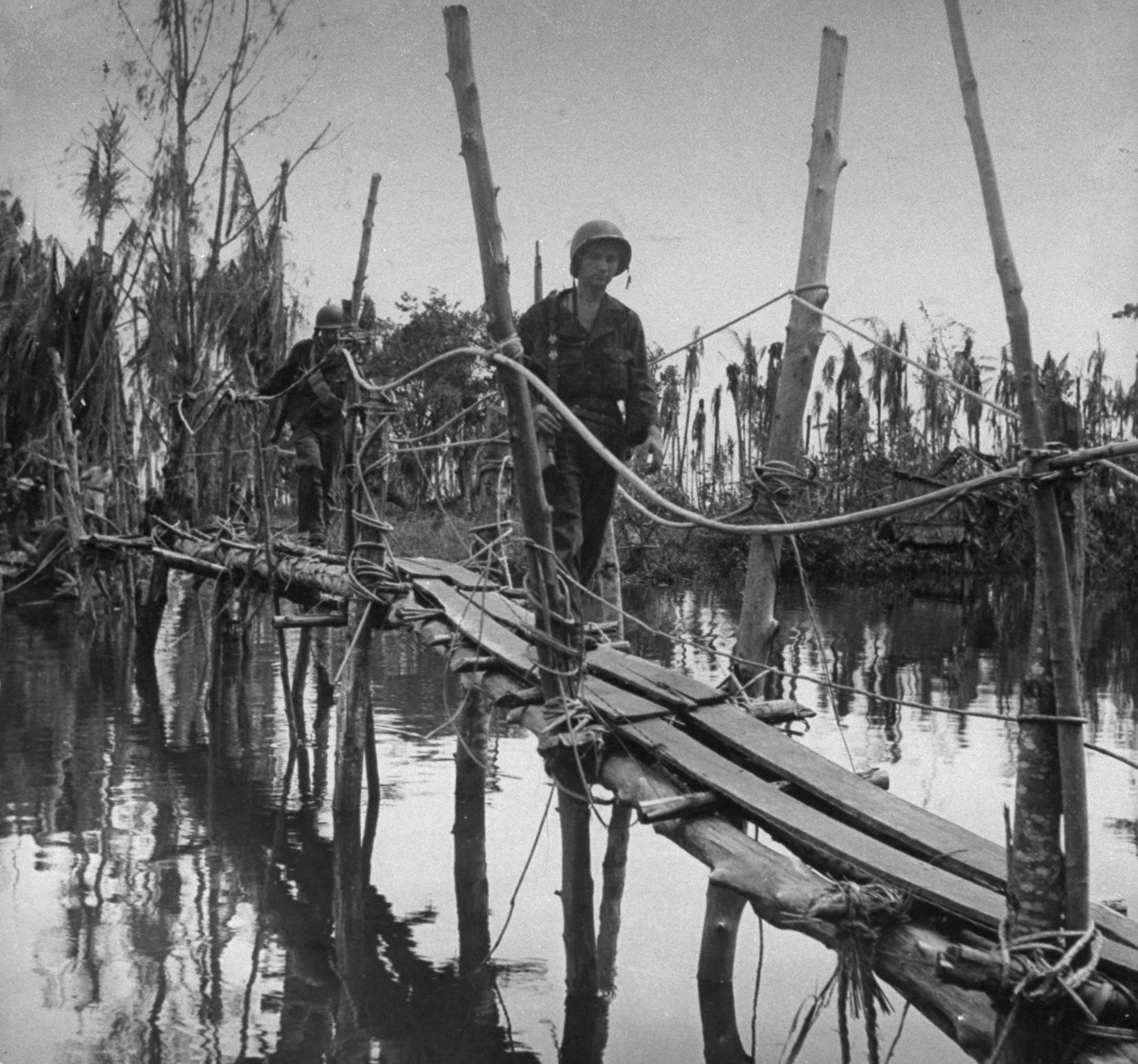 "Over Jap-built bridge walk Americans on patrol. It connects Entrance Creek Island with Buna Mission and one end of it was blown by Japs. Americans repaired it."