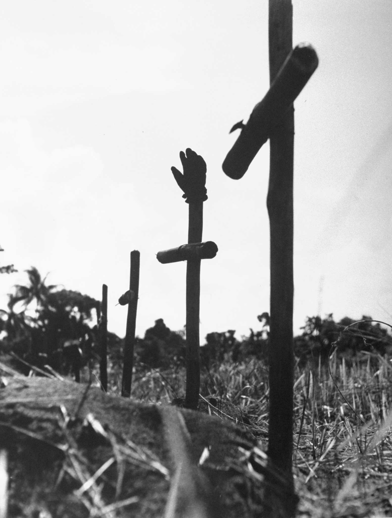 "A line of crude crosses marks American graves near Buna. A grave registrar's glove accidentally points toward the sky."