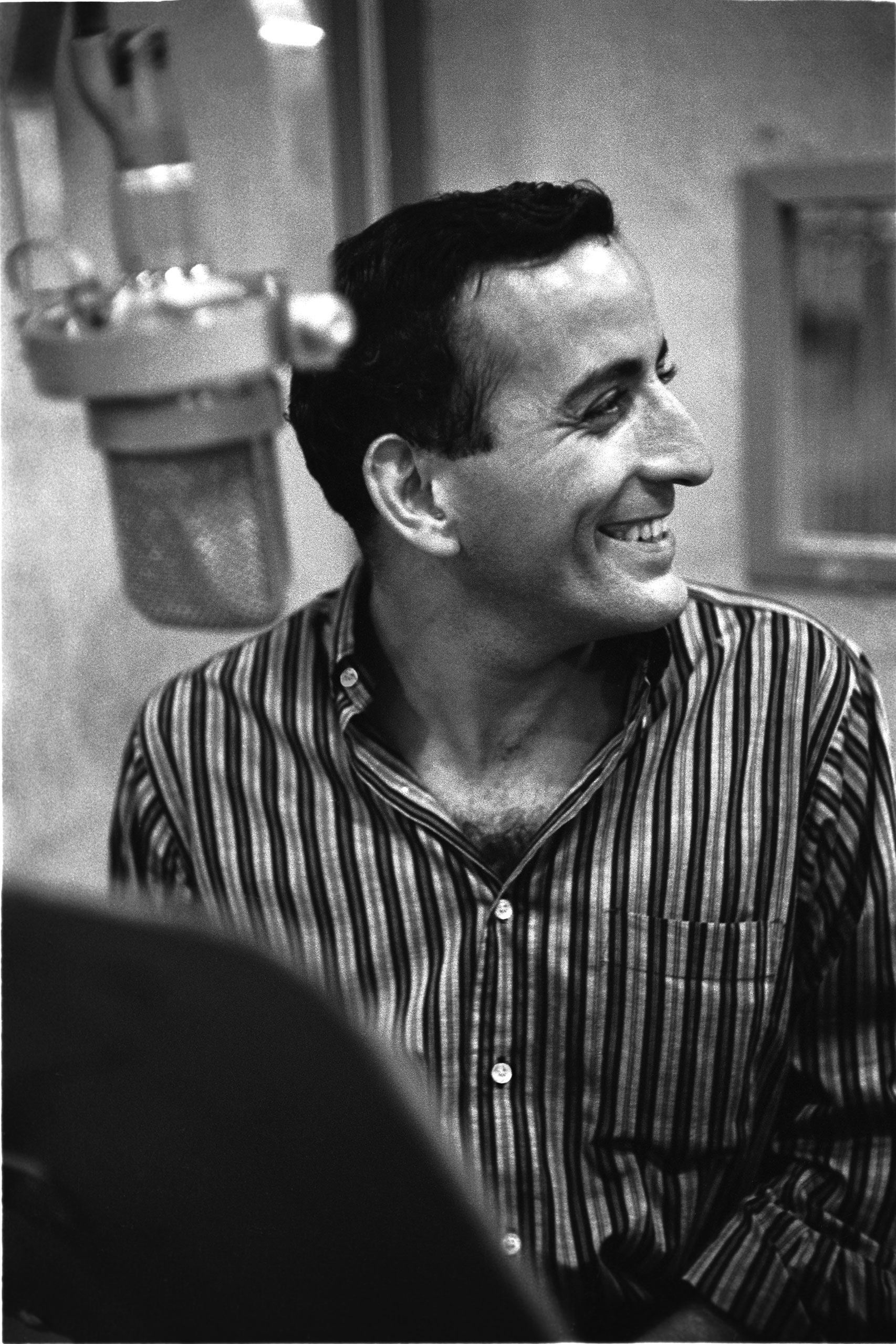 Tony Bennett in recording studio wearing long sleeved button down striped shirt. June 1957.