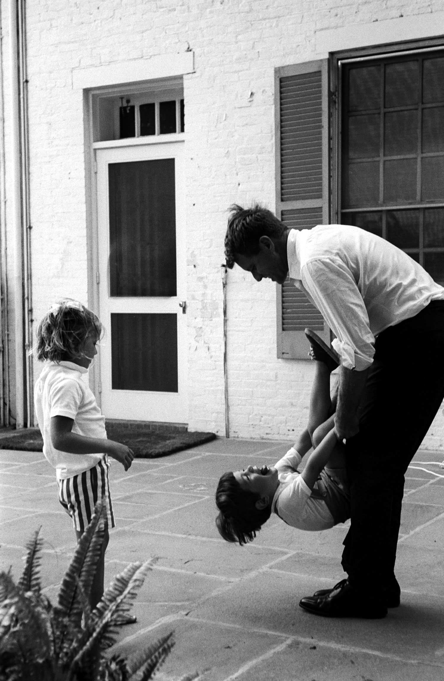 Bob swings his nephew on terrace. 'Jack made John the mischievous, independent boy he is,' says Jackie Kennedy. 'Bobby is keeping that alive.'