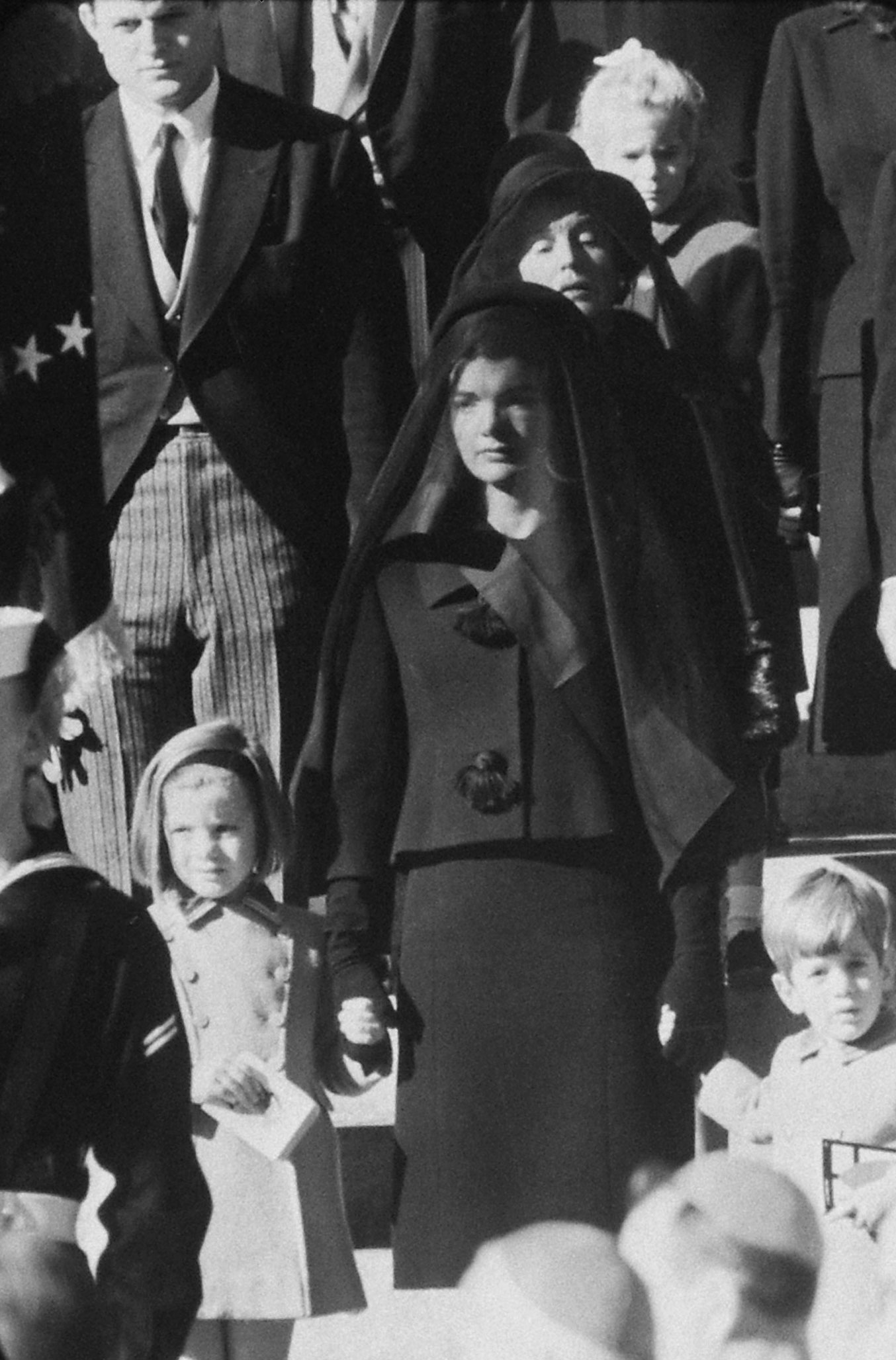 Wife. Mother. Niece. Three generations wait outside St. Matthew's for procession to cemetery. Behind Mrs. Kennedy stands the President's mother. Sydney Lawford, daughter of Kennedy's sister Pat, is at rear.