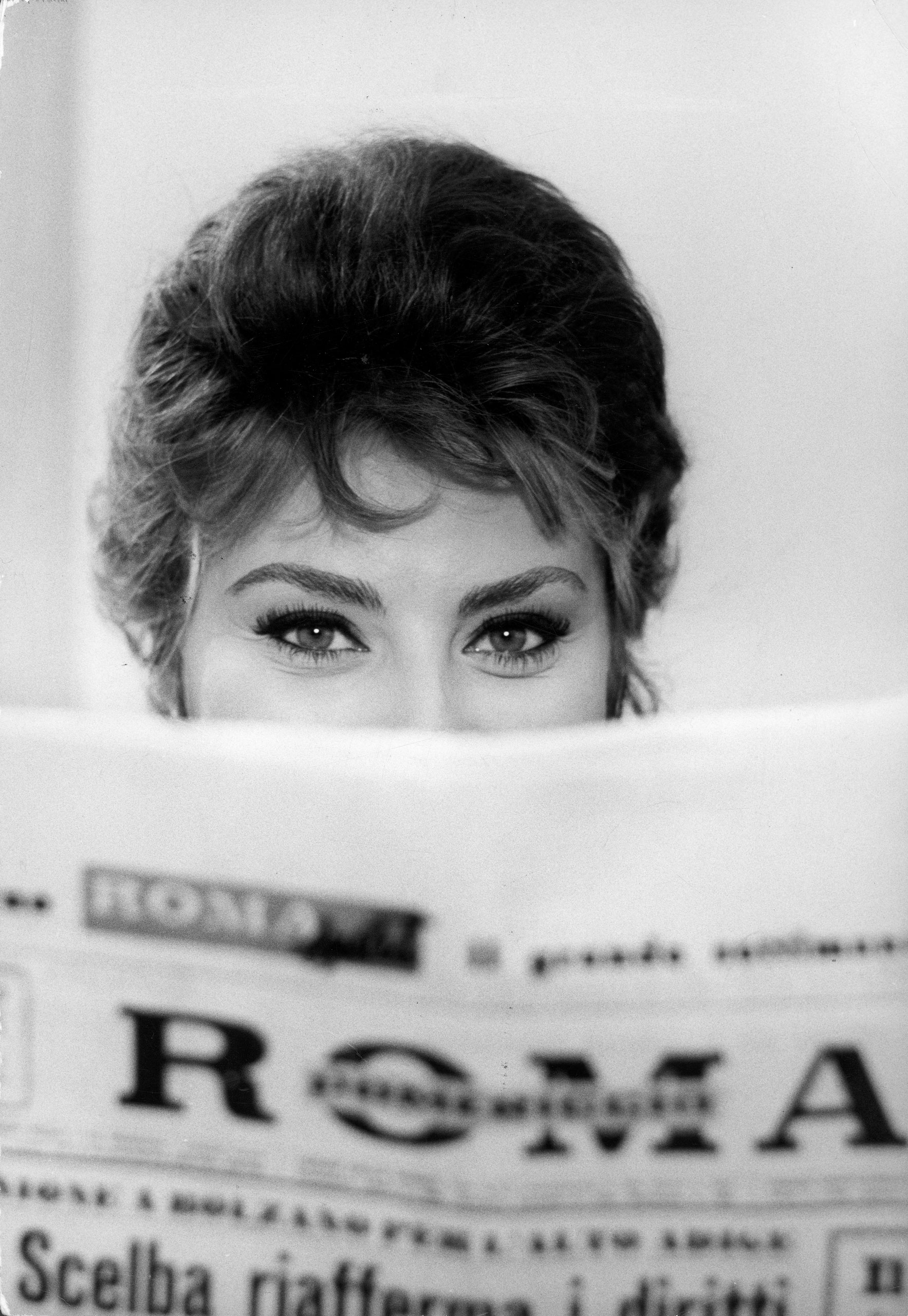 Sophia Loren impishly peering over the top of a newspaper.