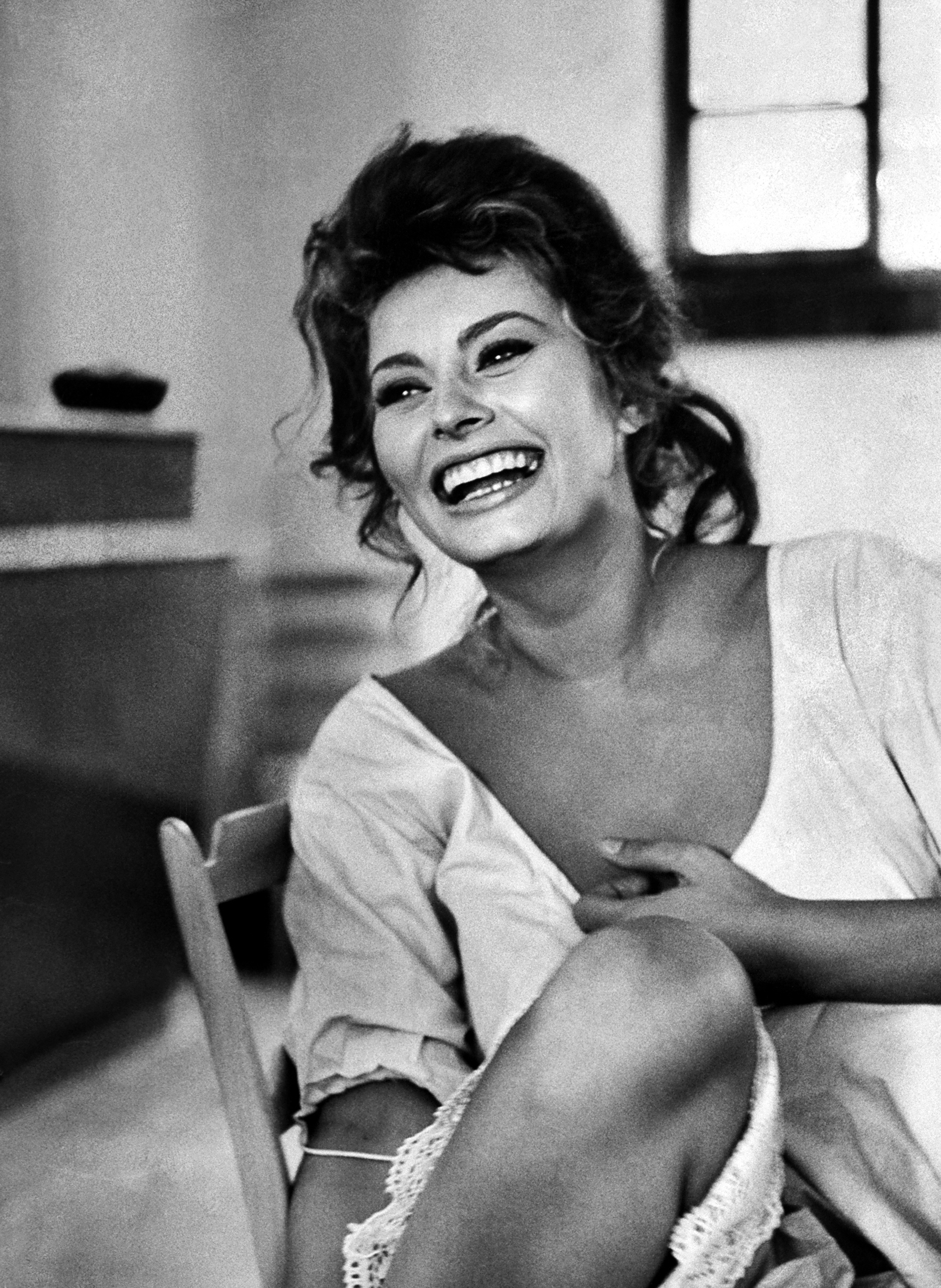 Sophia Loren laughing while exchanging jokes during lunch break on a movie set.
