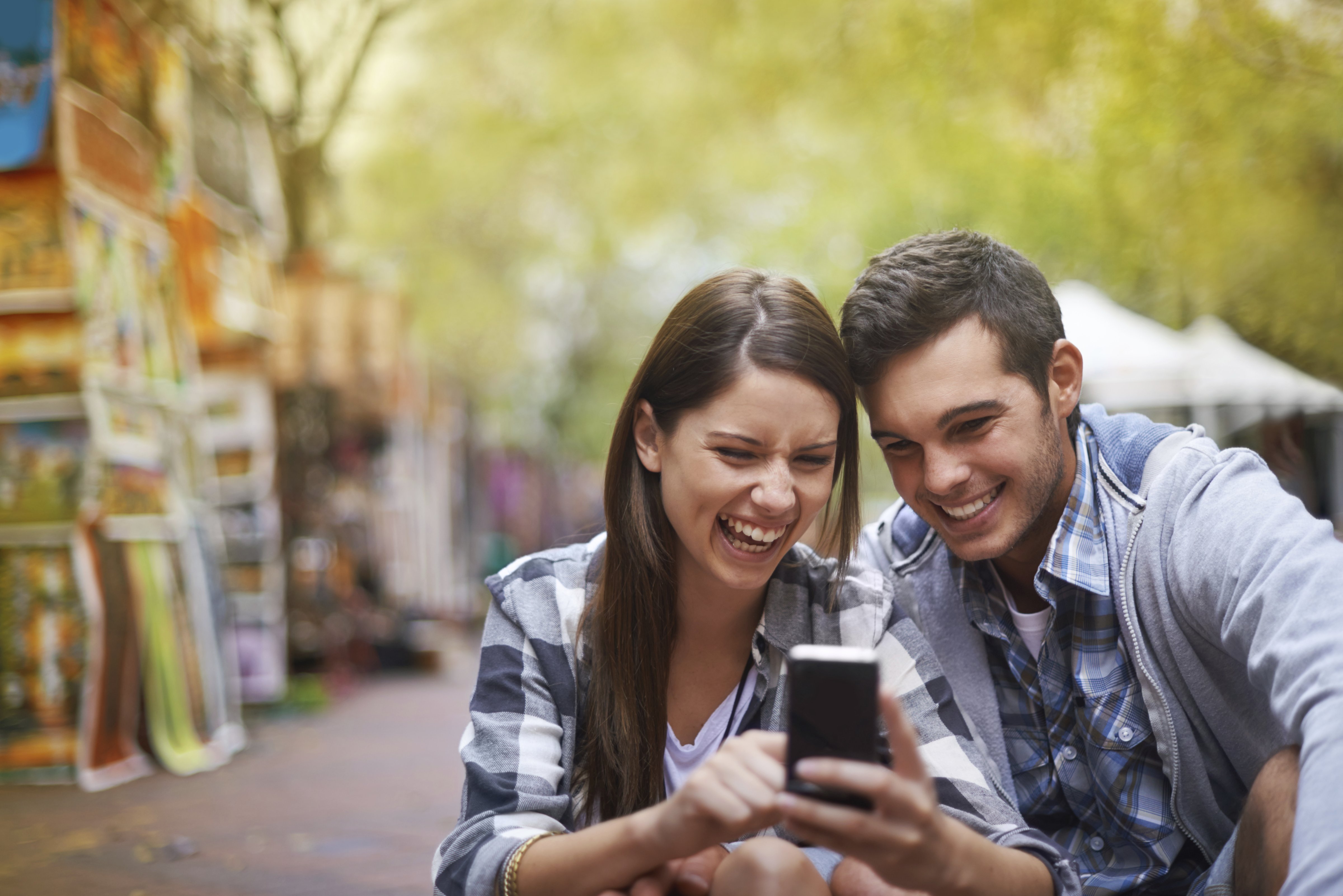 A young man and young woman share a laugh over a smartphone. (PeopleImages.com&mdash;Getty Images)