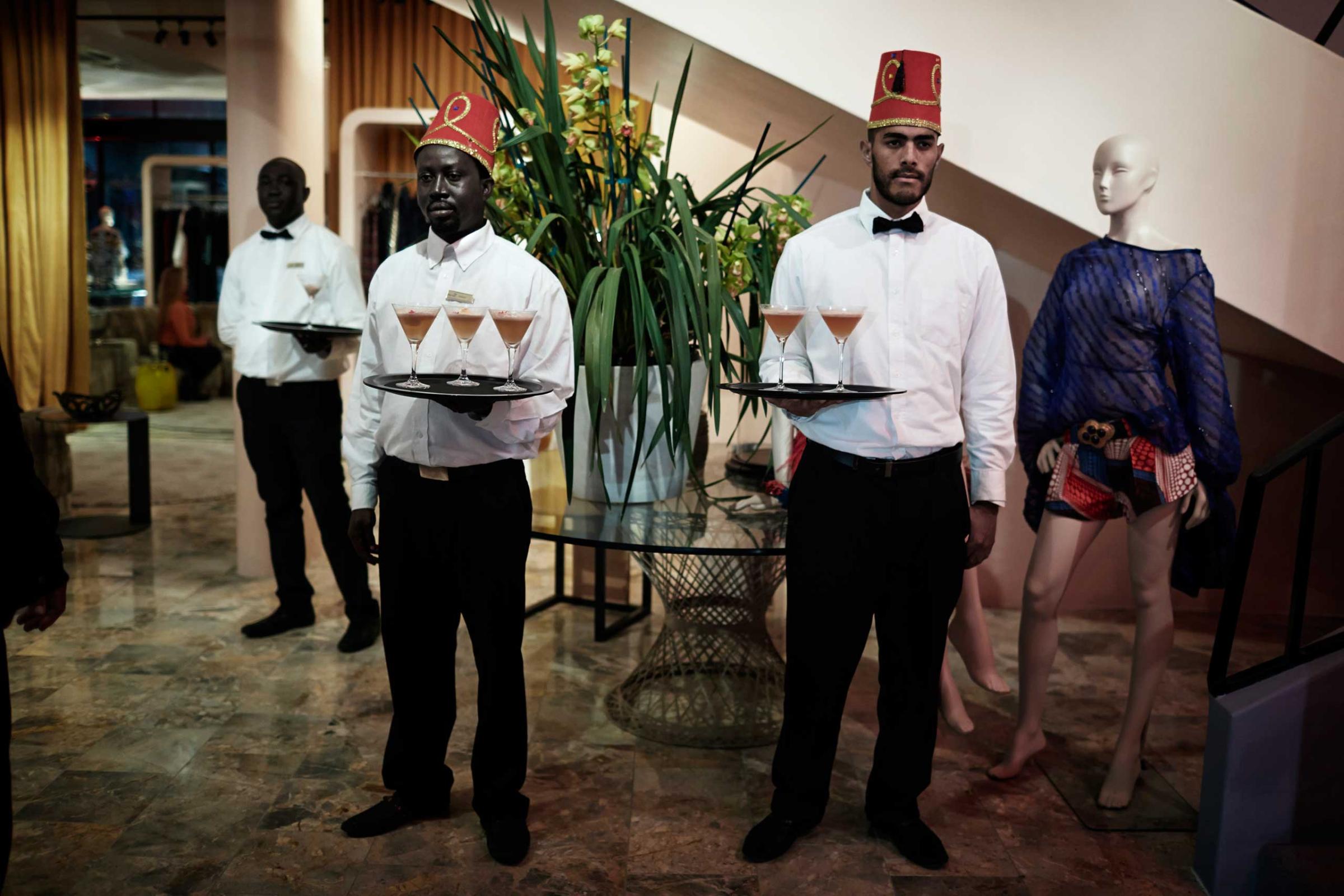 Waiters wait to serve drinks to guests before an installation show at the new Klûk CGDT flagship store during Mercedes-Benz Fashion Week on July 26, 2014, in Cape Town, South Africa.