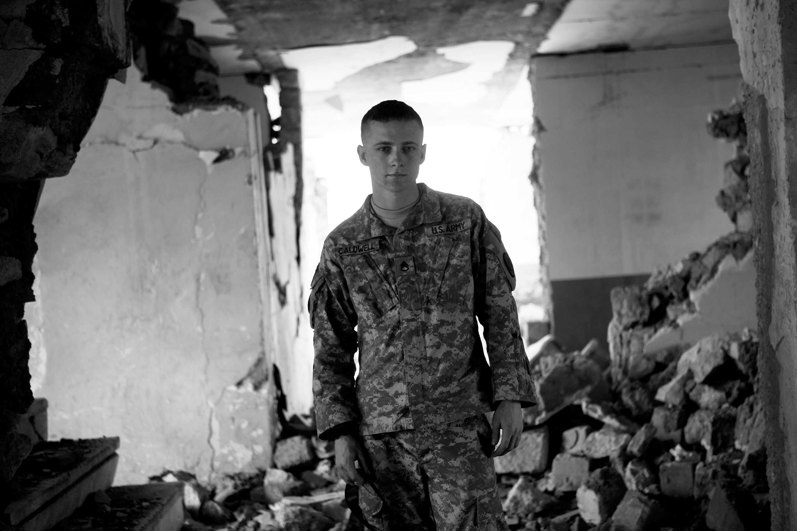 Sergeant Chad Caldwell.Maya Alleruzzo, March 30, 2008. Mosul, Iraq.
                              
                               We wanted to cover the daily lives of soldiers in Iraq’s most dangerous area. We chose Mosul - our stories referred to it then as al-Qaida’s last urban stronghold. On one of the first days living with the platoon, we asked soldiers to show us their good luck charms – the things they carried to keep them safe, grounded, connected.
                              
                              Staff Sergeant Chad Caldwell had nothing in his pockets but was eager to talk. 'I am my own good luck charm,' he said. 'I am what keeps me alive. They’ve tried to blow me up, shoot me, throw hand grenades at me, everything they can throw at me. This far I have walked away without a scratch on me, knock on wood.' Then he smirked. 'I am Superman. I cannot be defeated. I am invincible.'
                              
                              Now it was time for a portrait. He stepped into the center of the room in the partially destroyed building we were using as a studio.
                              
                              He was slight, wiry – barely taller than me.  But he stood tall. He looked like a boy, barely old enough to shave, but he’d fought in Iraq three times. He gazed into my lens as the sun filtered through the rubble, backlighting him. He looked, in this light, in this place, like a ghost. I drew in my breath and pressed the shutter.
                              
                              He was killed exactly one month later by a bomb during a foot patrol. His death shook me. Sometimes, irrationally, I still worry that this photograph, or talking to him about his invincibility, was the thing that broke his lucky streak.