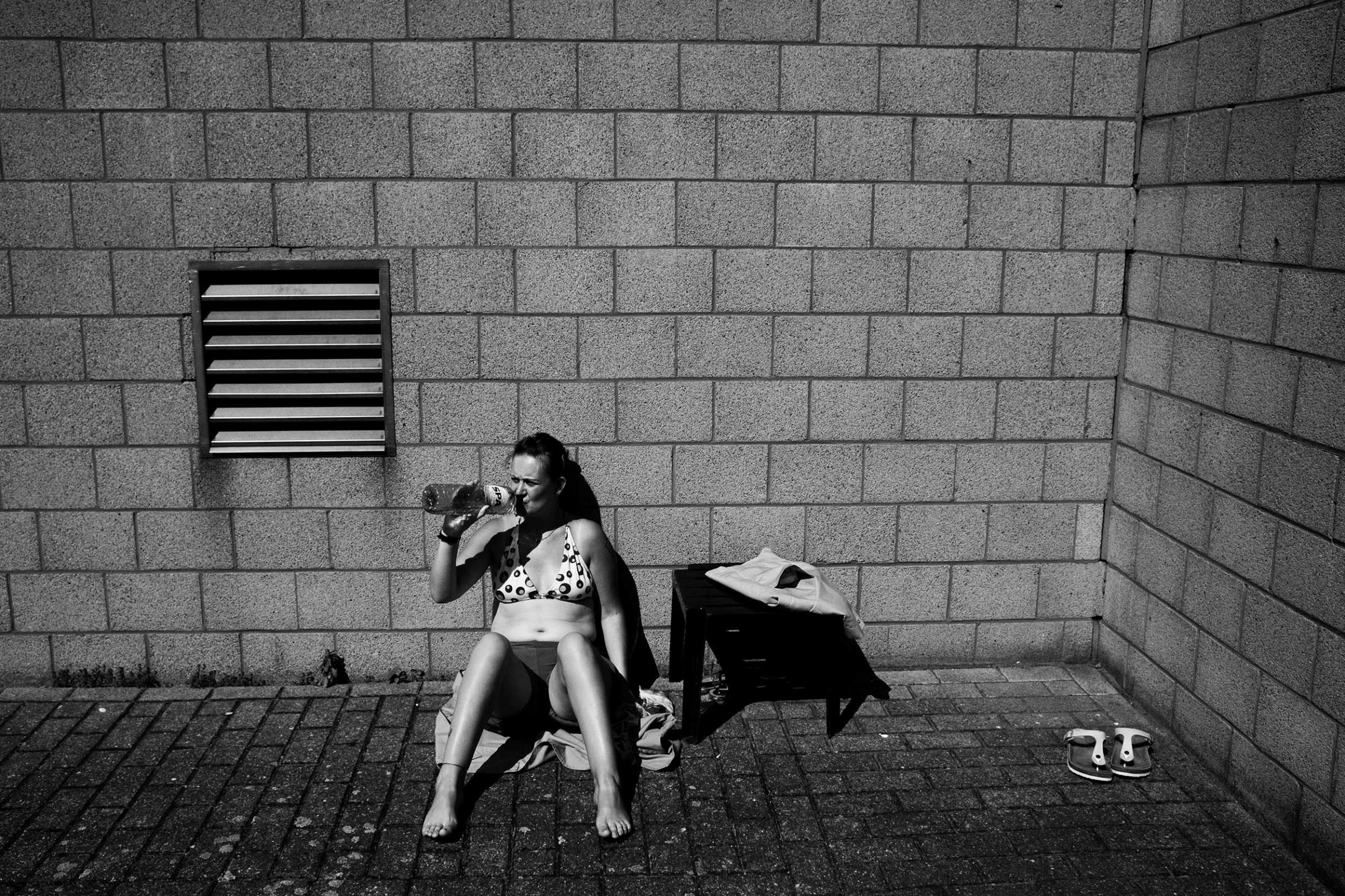 A female prisoner sunbathing at the women's prison in Berkendaele, Brussels. This courtyard is located next to a prison for men, whose cells offer a direct view on the women's courtyard. Some of the women enjoy mocking the men or exposing themselves to them. Brussels, Belgium. July 2011.
