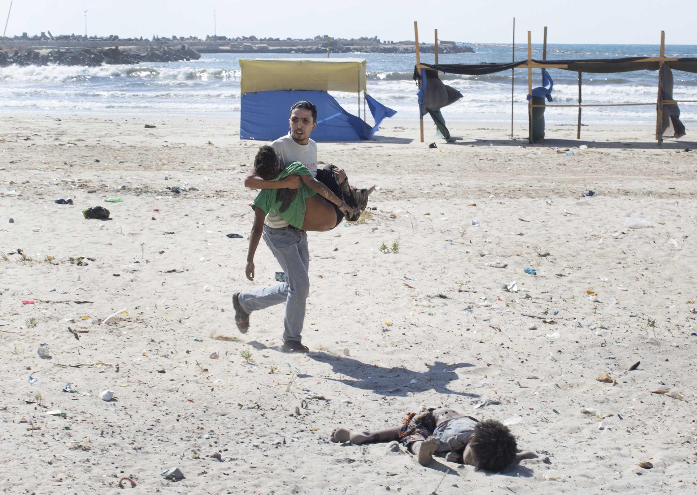 A man carries a child as another lies dead after two explosions on a beach in Gaza, July 16, 2014.