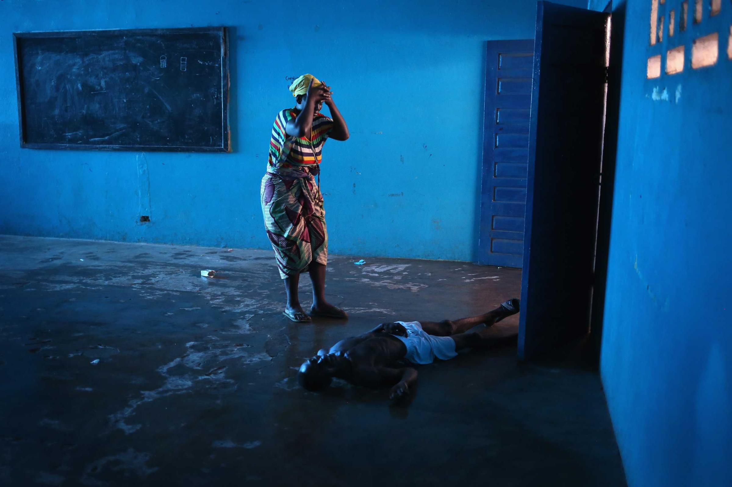Umu Fambulle stands over her husband Ibrahim after he staggered and fell knocking him unconscious, in an Ebola ward in Monrovia, Liberia., Aug. 15, 2014.