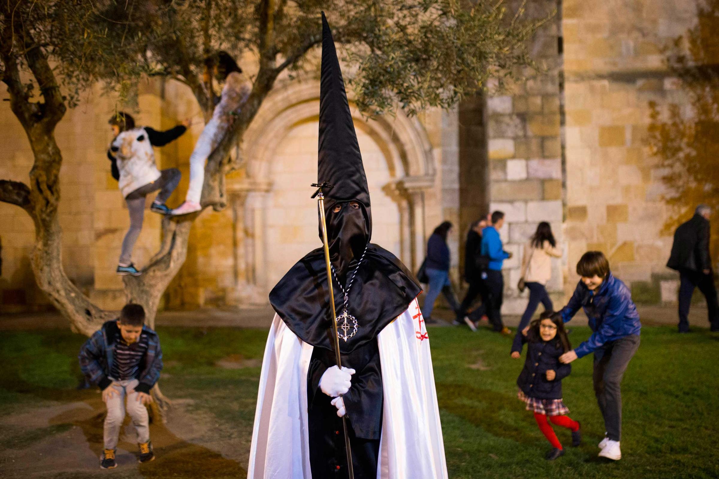 Children play in the background as a penitent watches a march in Zamora, Spain, April 14, 2014.