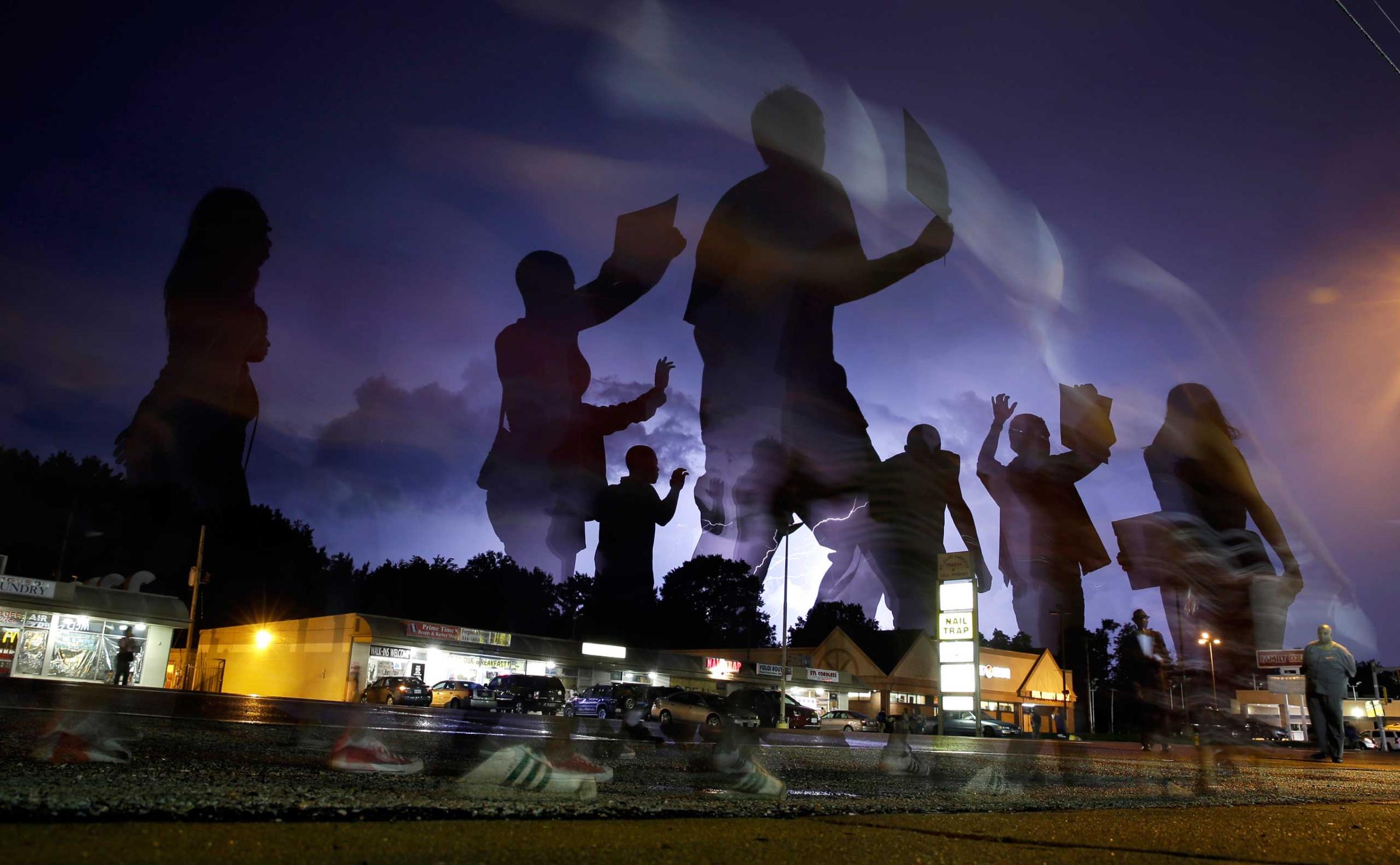 Protesters march in the street as lightning flashes in the distance in Ferguson, Mo, Aug. 20, 2014.