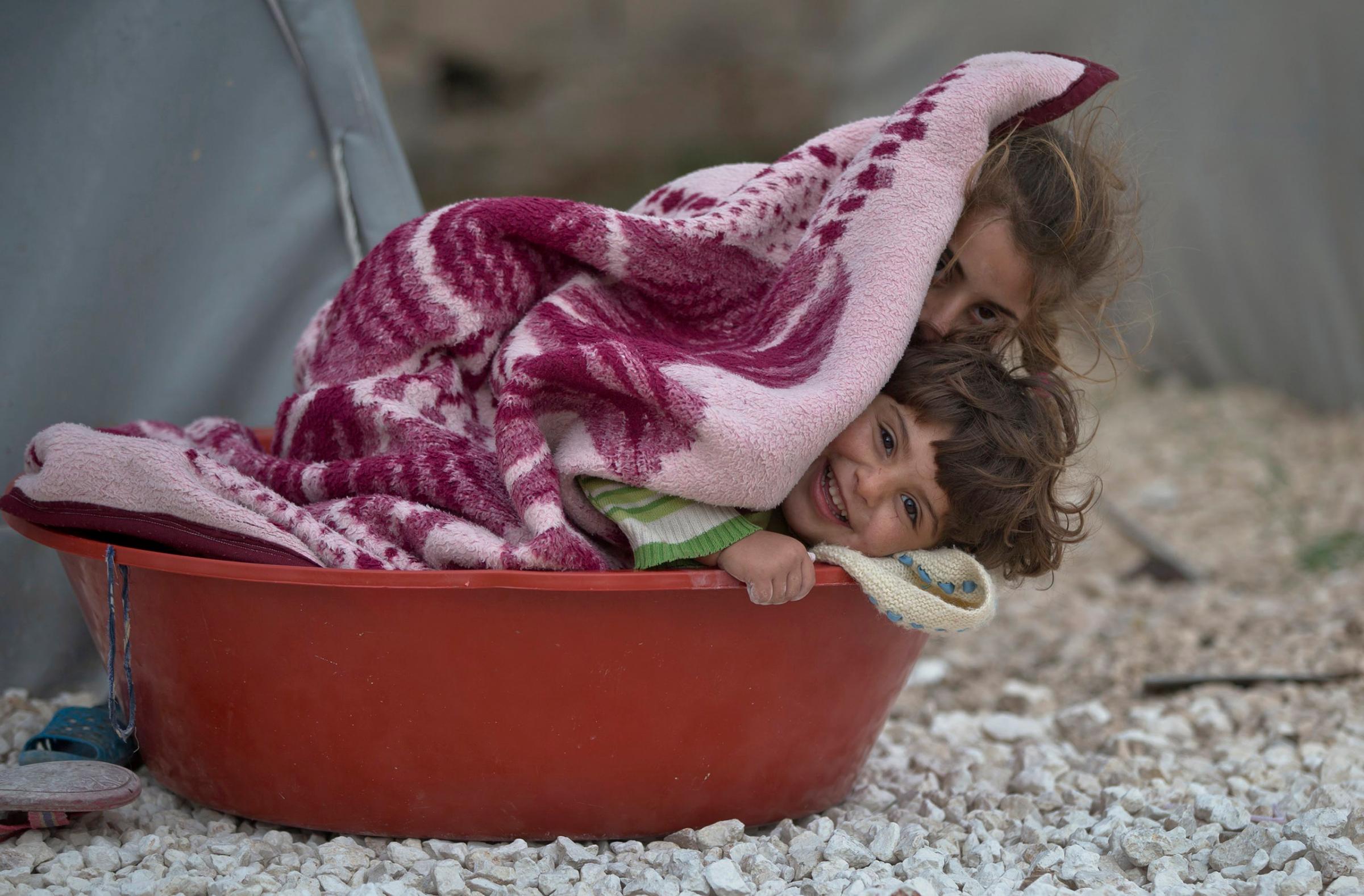 Syrian Kurdish refugee children from the Kobani area cover themselves in a blanket on a cold morning at a camp in Suruc, on the Turkey-Syria border on Nov. 16, 2014.