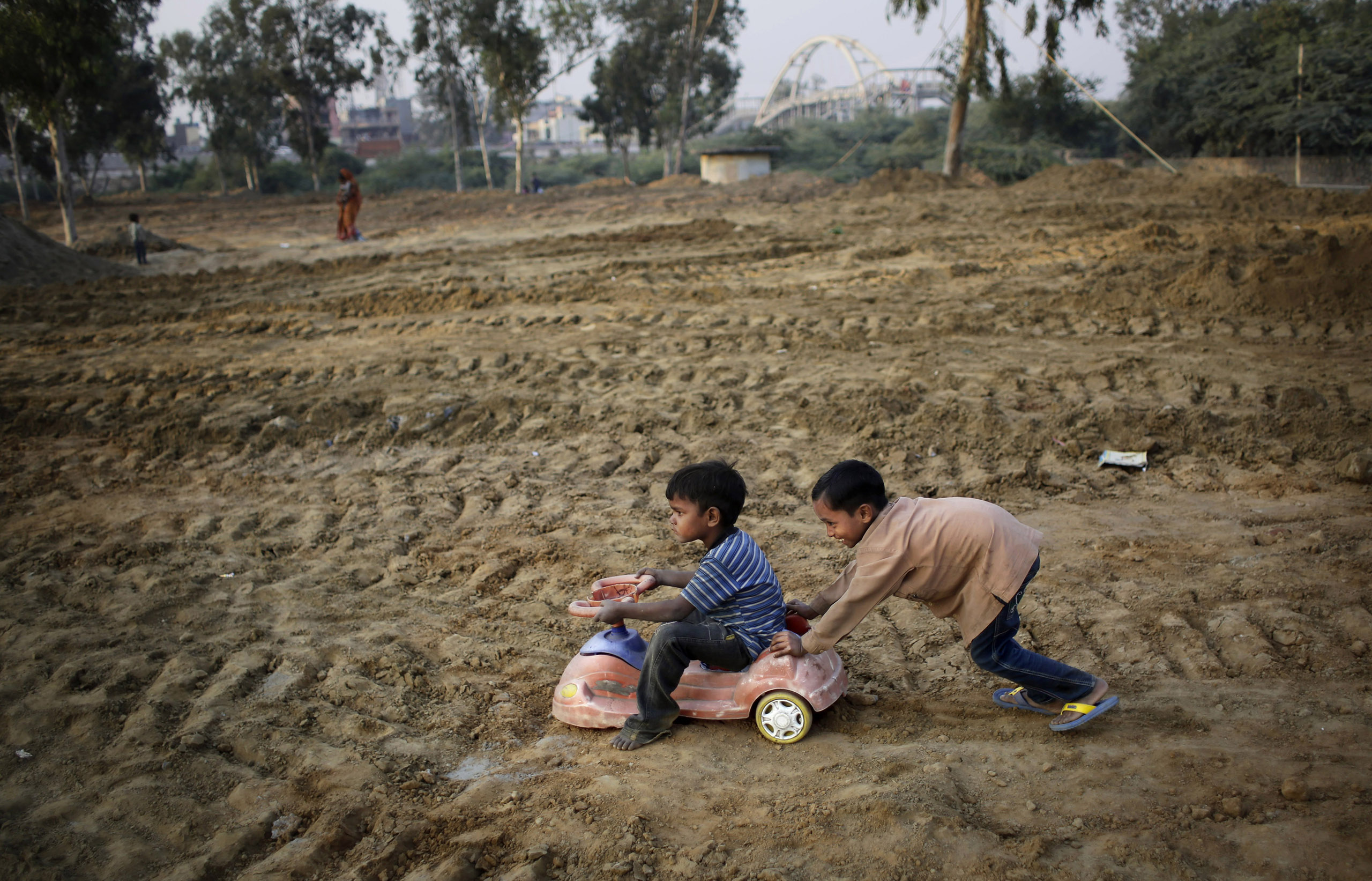 Indian boys play with a toy car salvaged from a nearby landfill in a field being prepared for a metro station near a slum in New Delhi, India on Nov. 13, 2014.