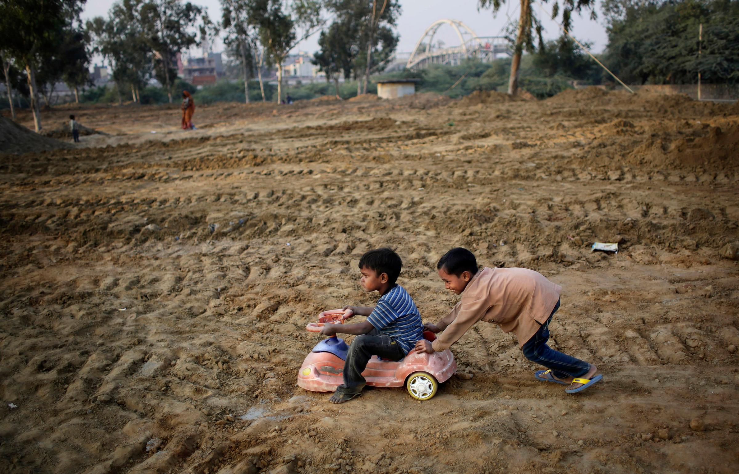 Indian boys play with a toy car salvaged from a nearby landfill in a field being prepared for a metro station near a slum in New Delhi, India on Nov. 13, 2014.