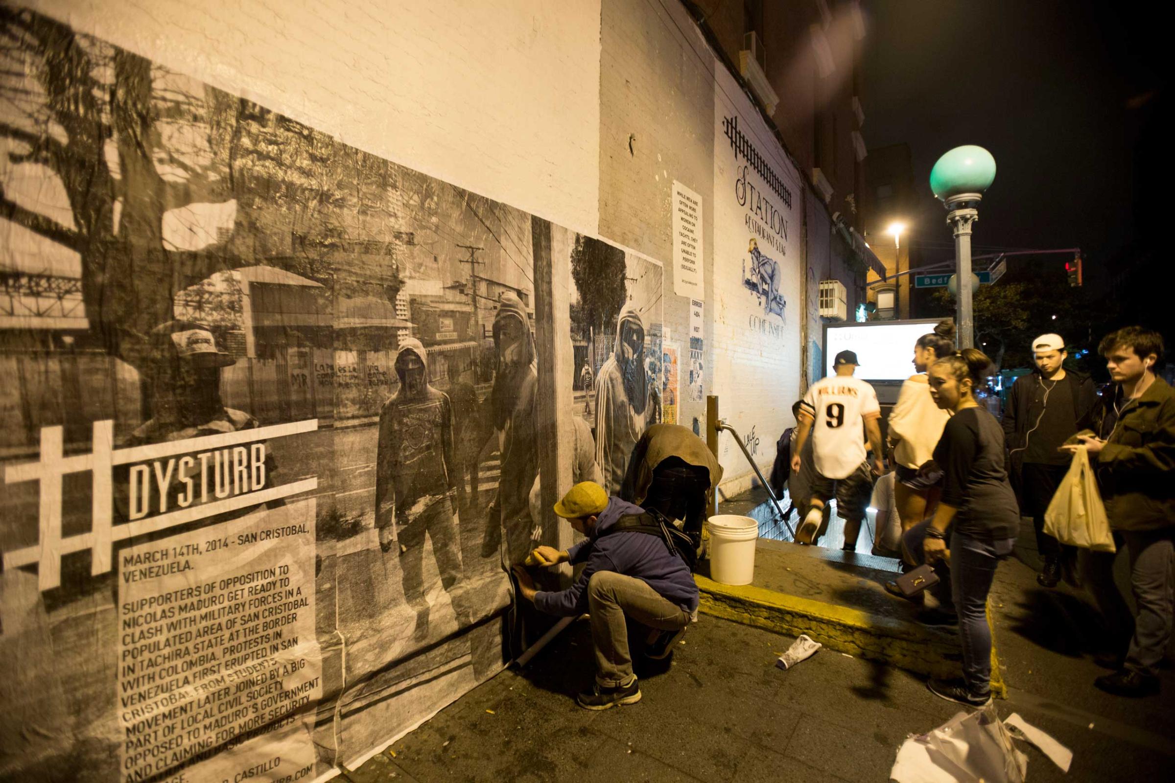 Onlookers, as the Dysturb team paste a photograph in Brooklyn, New York (on the corner of N 7th Street and Bedford Avenue). October 16th 2014.