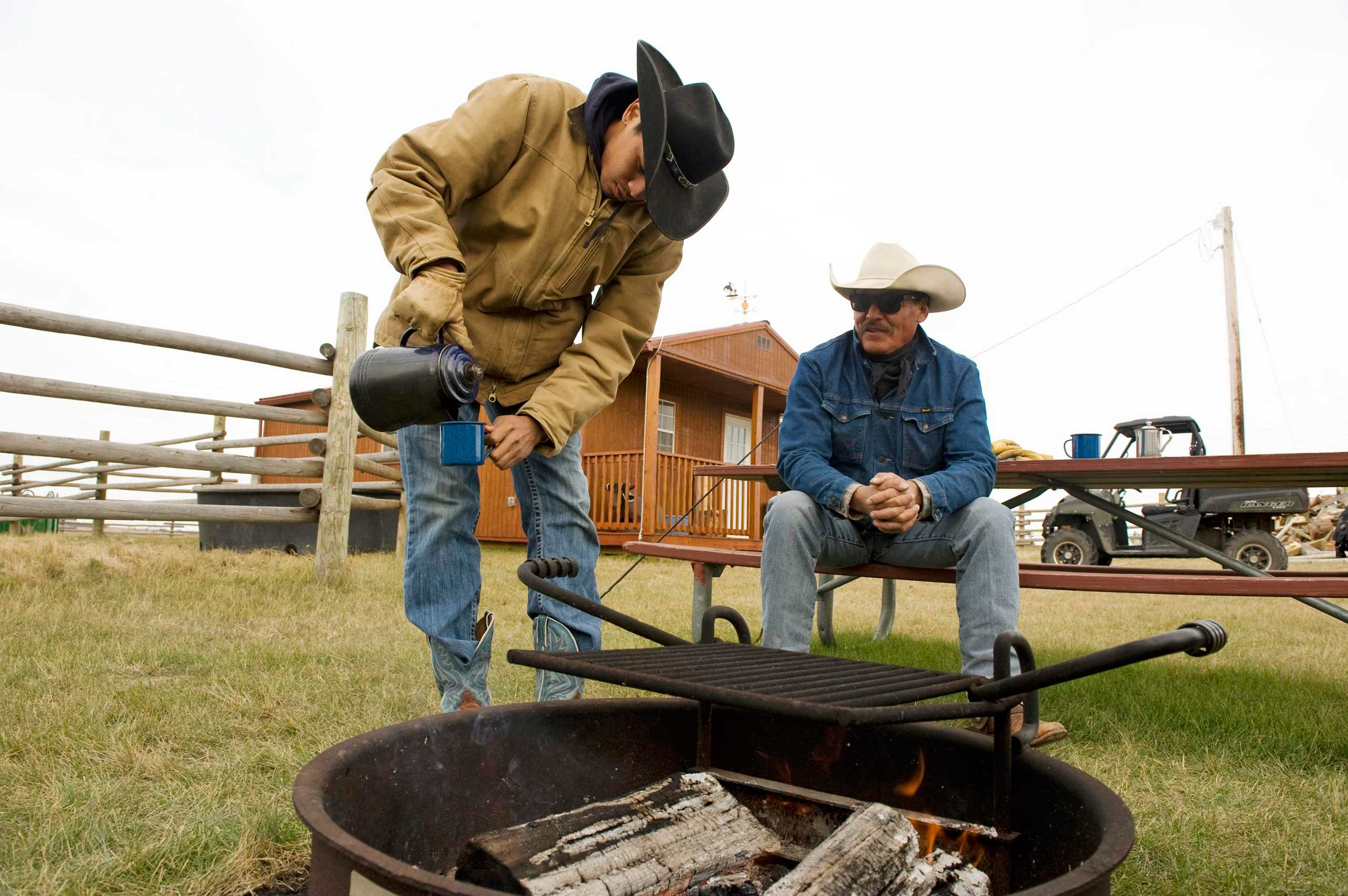 Jesse Bear (L) and his father, Sonny James Bear, Three Affiliated Tribes members, drink coffee over the campfire during a break from training horses on their ranch just off the Fort Berthold Reservation in N.D. on Nov. 1, 2014.